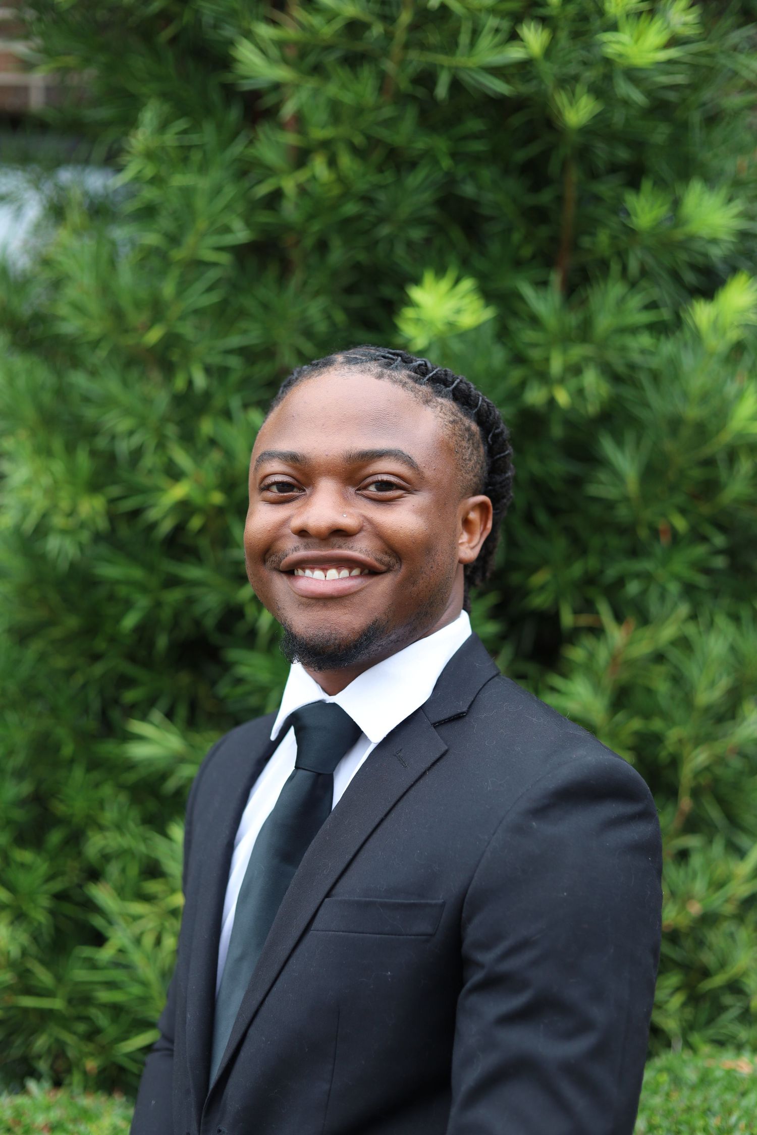 Headshot image of a young man wearing a black formal suit and tie