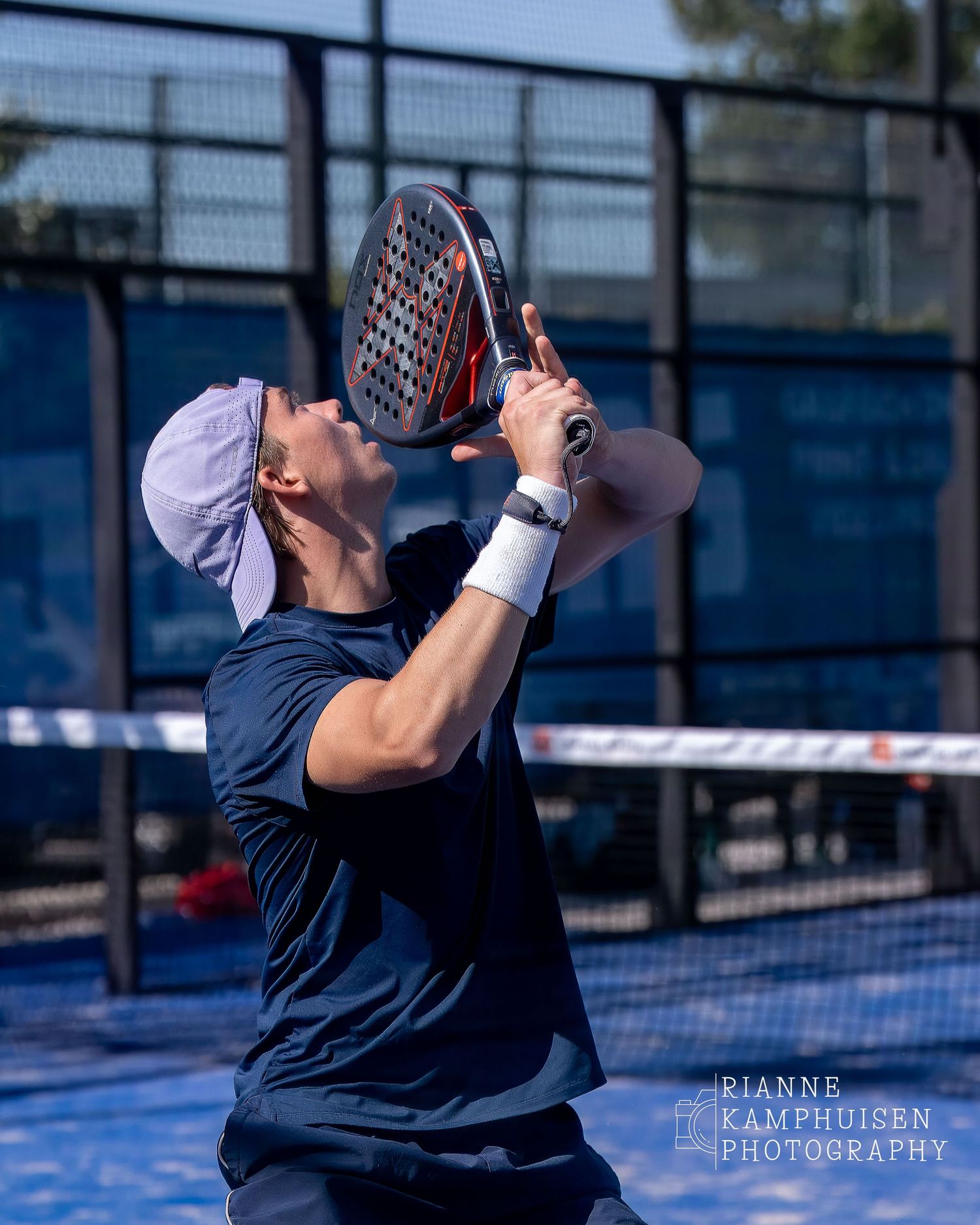 Padelspeler met een blauwe pet achterstevoren op zijn hoofd staat klaar om een smash te slaan