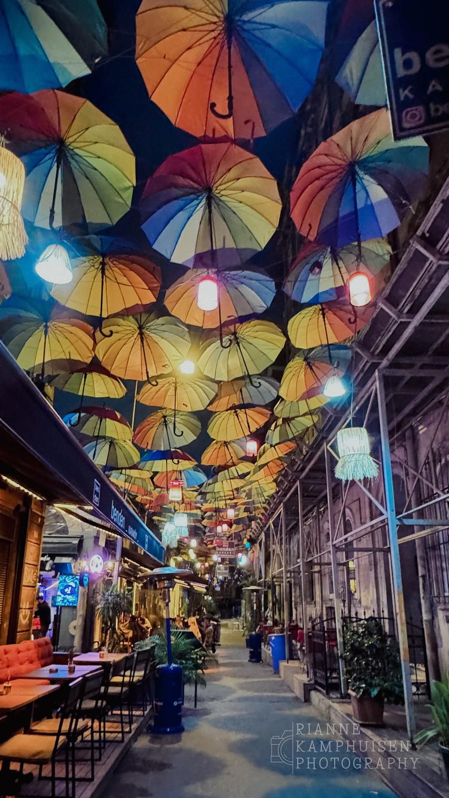Smalle steeg met kleurrijke hangende paraplu’s als dak, sfeervol verlicht in de avond. Istanbul, Turkije