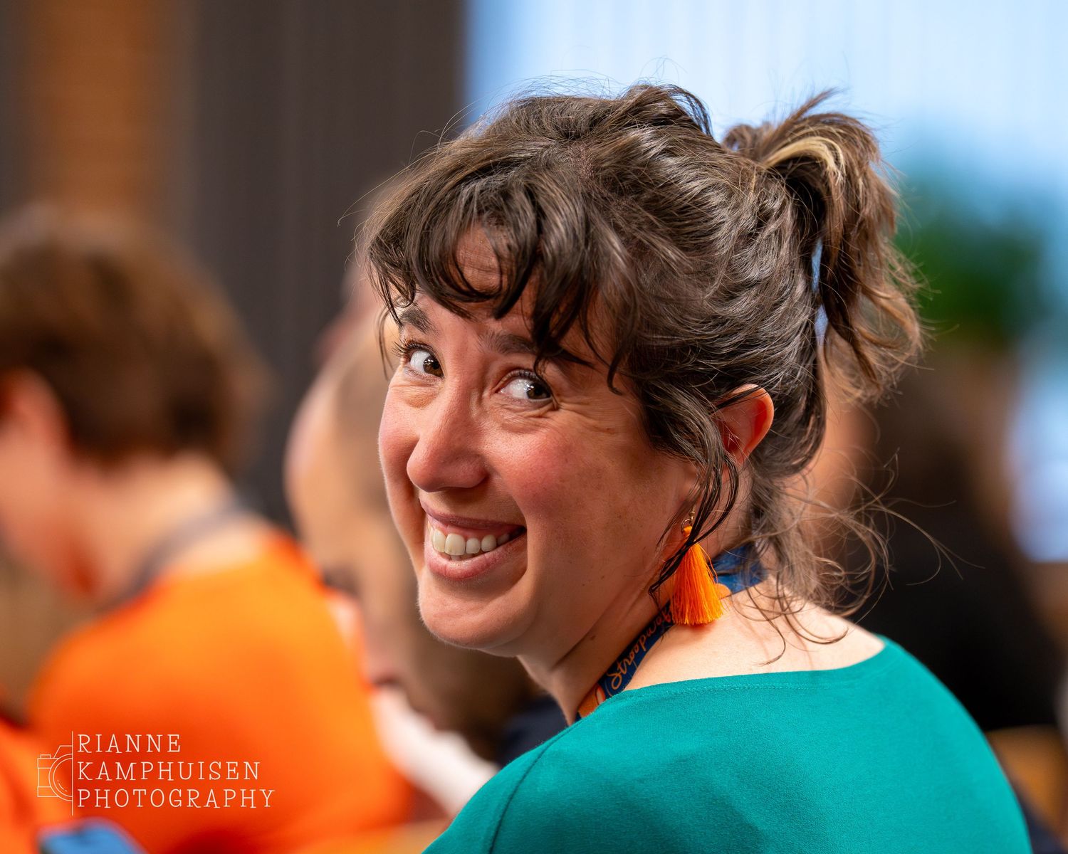 Vrouw kijkt lachend over haar schouder naar de camera, met oranje oorbellen en een vrolijke blik.