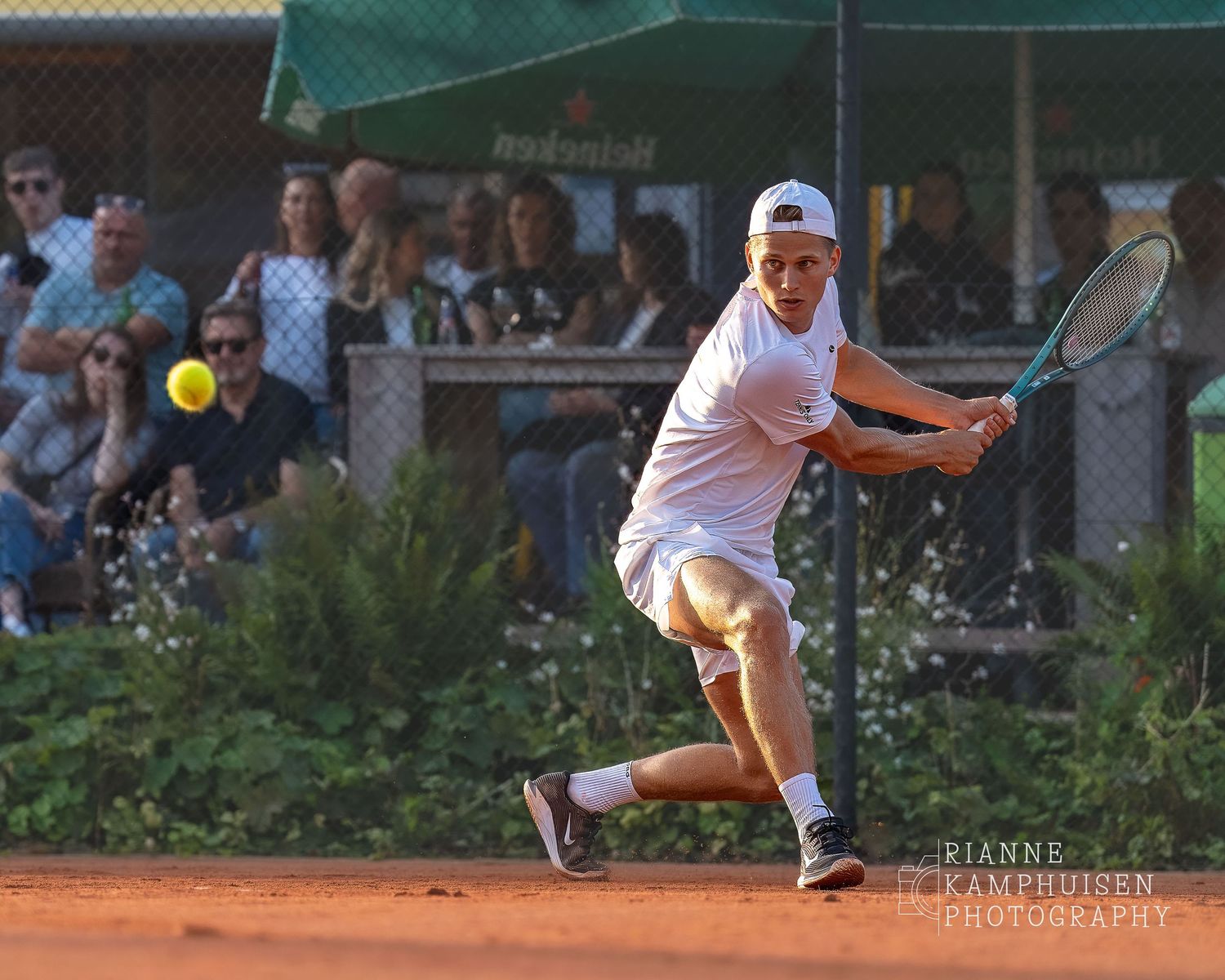 Actiefoto's van de woensdagavond van eengravel tennistoernooi met spelers in actie, dubbelspel, toeschouwers en zomerse sfeer rond de baan.