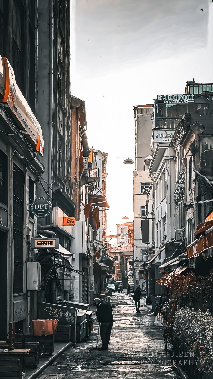 Rustige straat met oude gevels en lichtreclames bij zonsopgang, met een paar mensen in de verte. Istanbul, Turkije