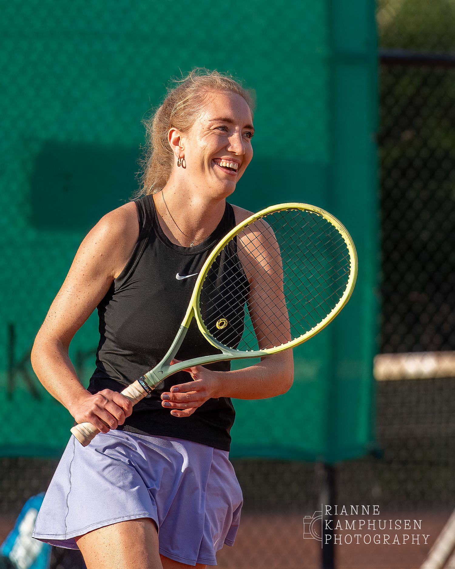 Actiefoto's van de vrijdagavond van een gravel tennistoernooi met spelers in actie, dubbelspel, toeschouwers en zomerse sfeer rond de baan.