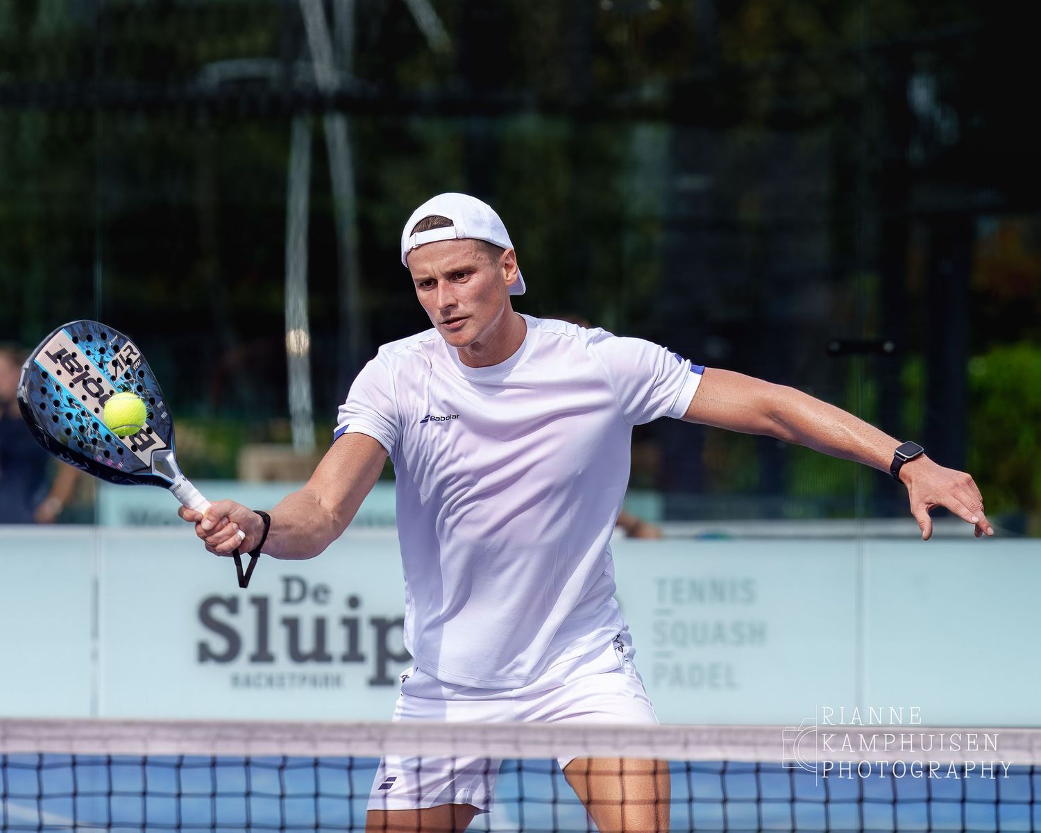 Padelspeler met pet achterstevoren op slaat een volley op een parelbaan