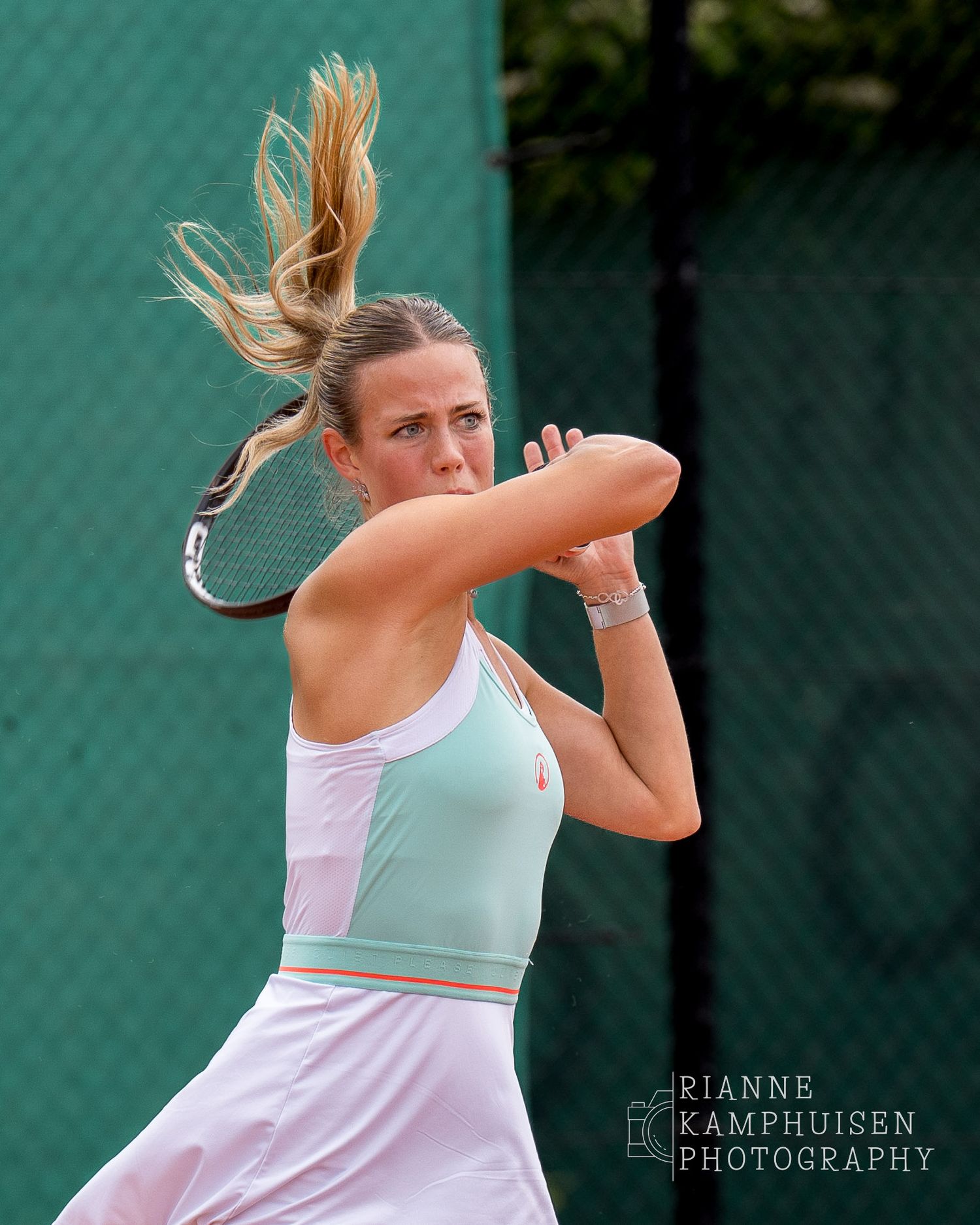 Tennisster in mintgroene en roze outfit voert een krachtige forehand uit, haar haar zwaait mee in de beweging.