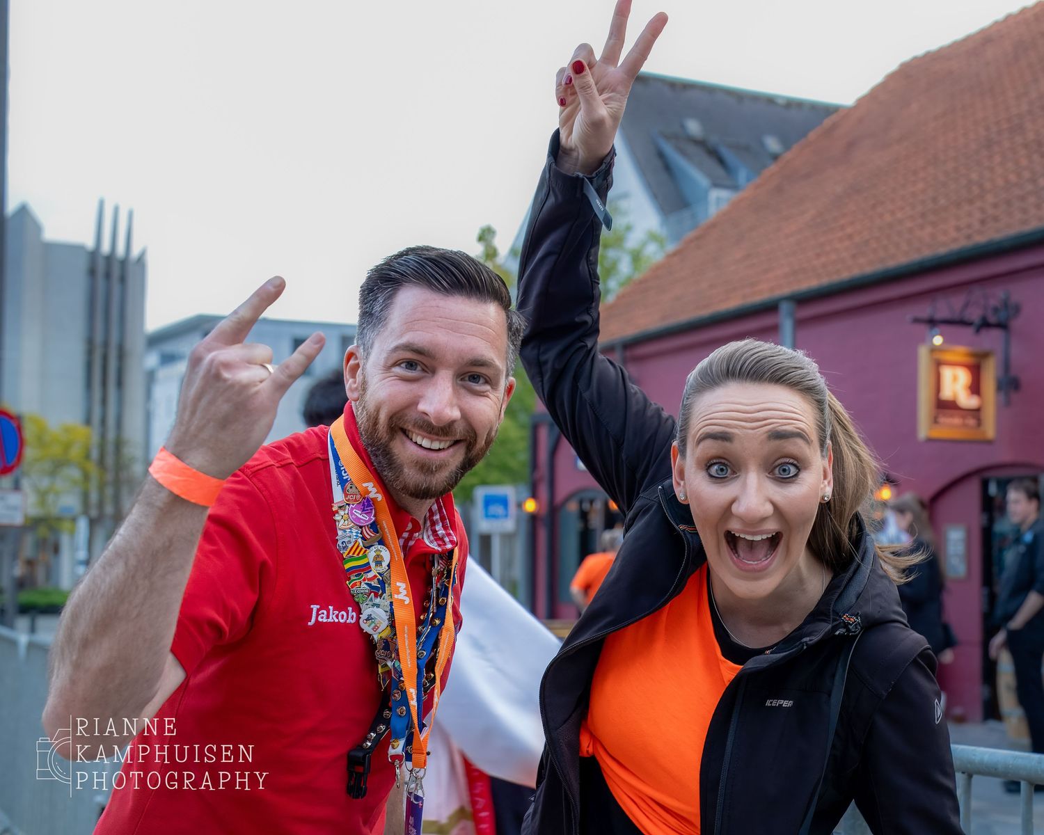 Twee enthousiaste deelnemers poseren lachend voor de camera met handen in de lucht tijdens een evenement in de stad.