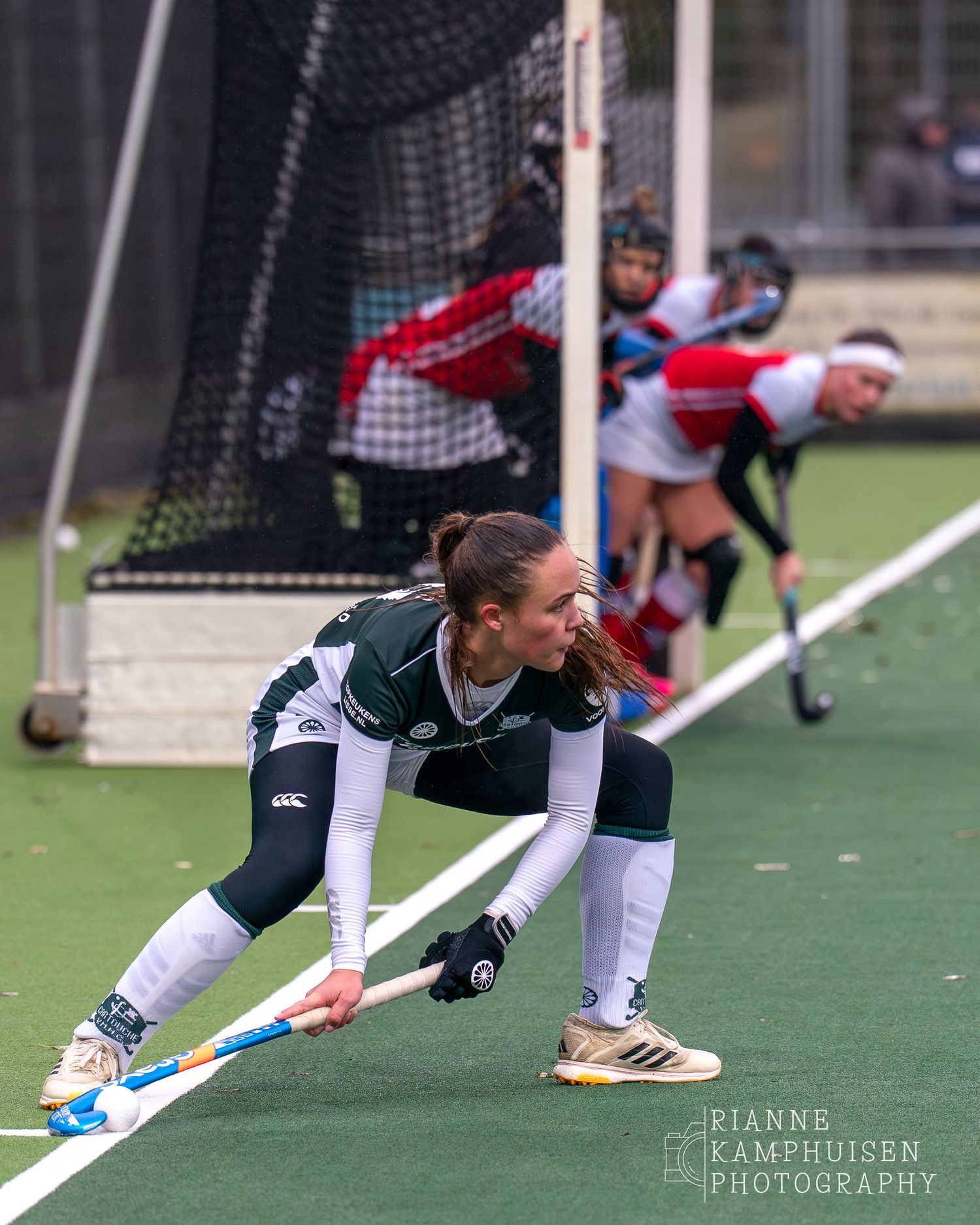 Hockeyspeelster staat klaar voor een strafcorner. Op de achtergrond zie je te tegenstanders in het doel staan om te verdedigen .