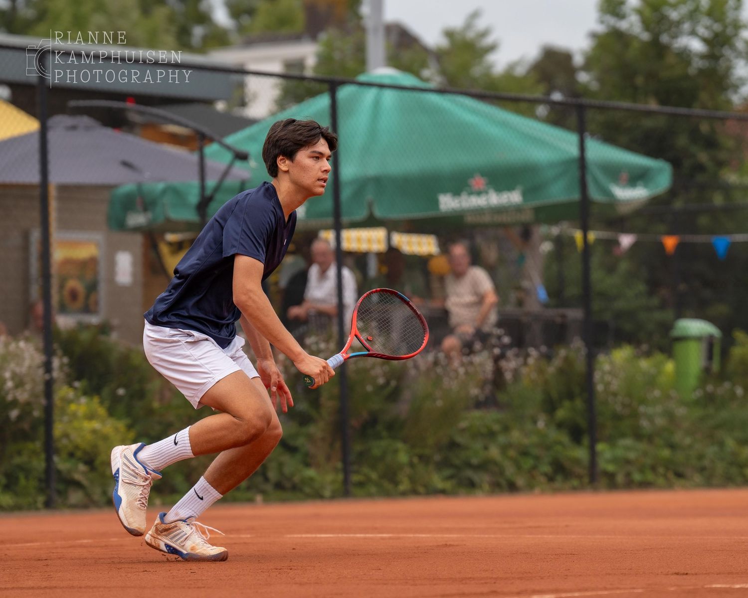 Actiefoto's van gravel tennistoernooi met spelers in actie, dubbelspel, toeschouwers en zomerse sfeer rond de baan.