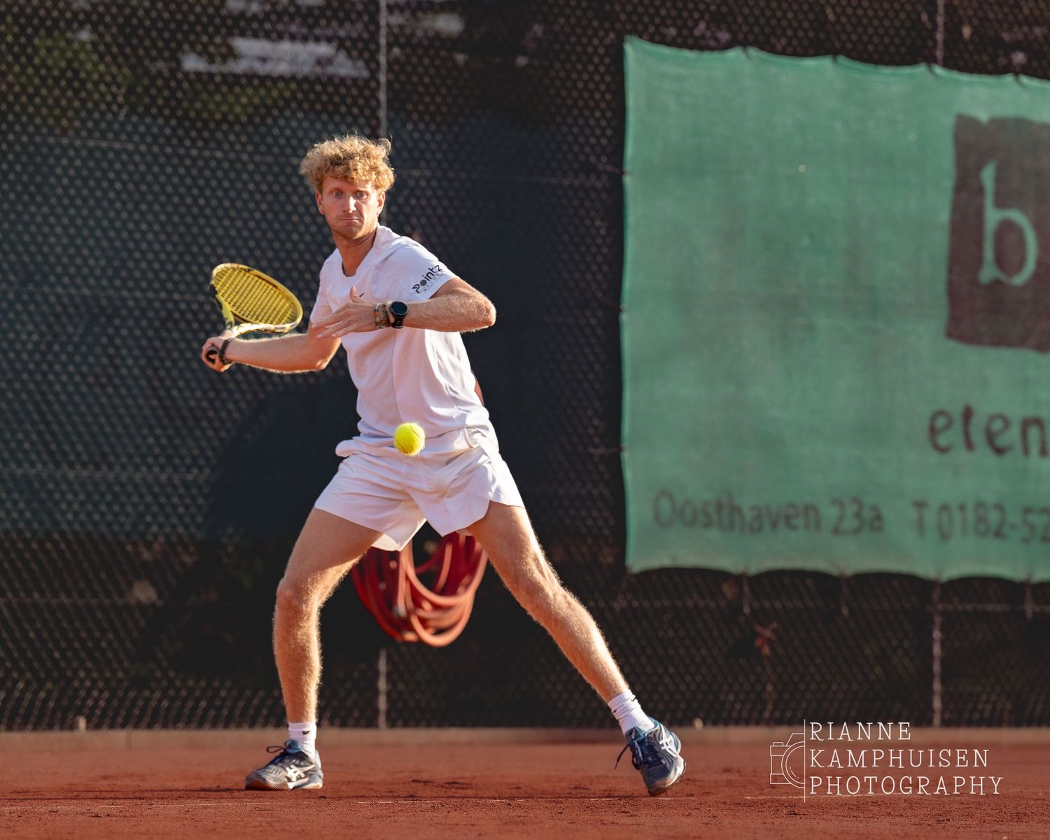 Actiefoto's van de vrijdagavond van een gravel tennistoernooi met spelers in actie, dubbelspel, toeschouwers en zomerse sfeer rond de baan.