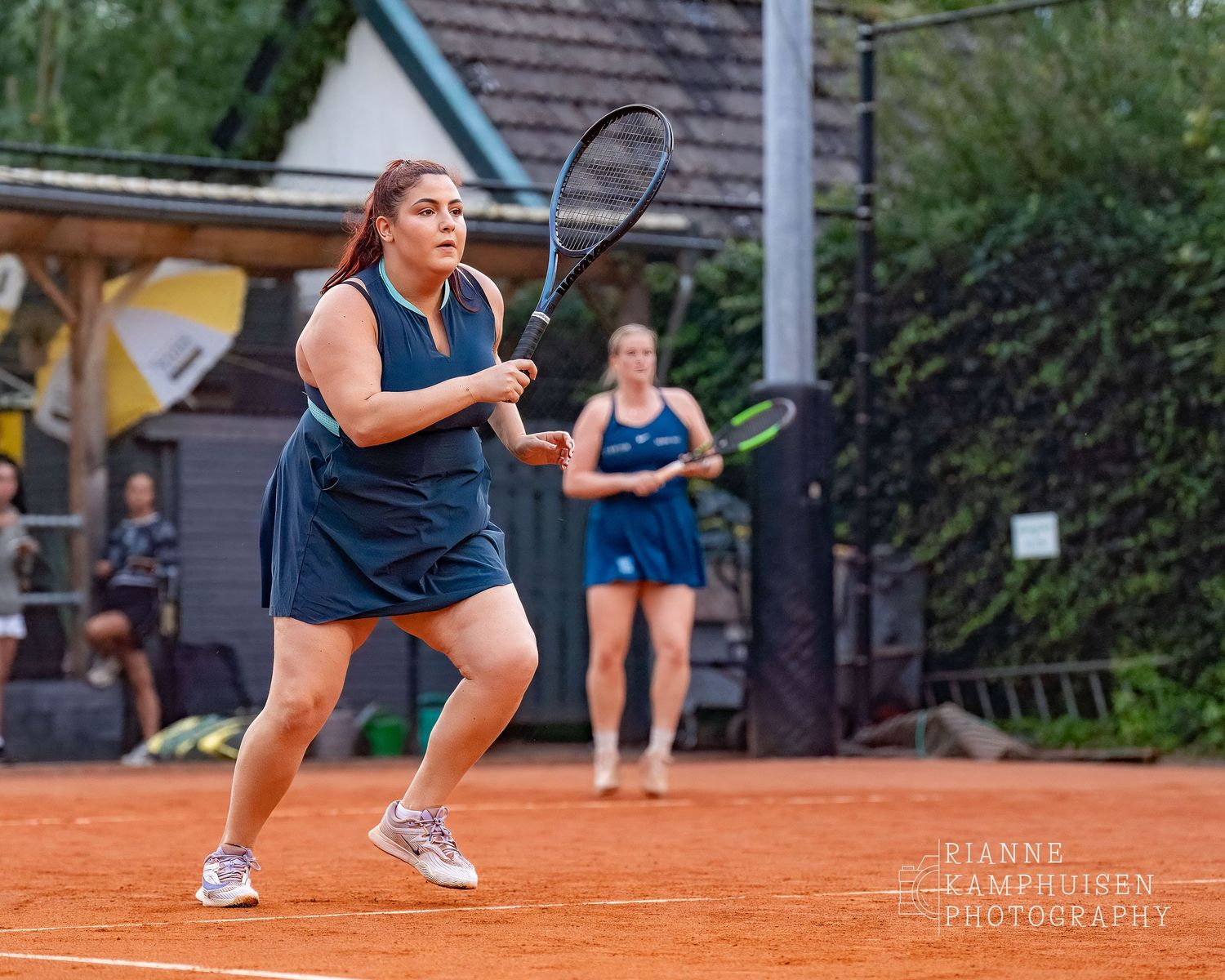 Actiefoto's van de woensdagavond van eengravel tennistoernooi met spelers in actie, dubbelspel, toeschouwers en zomerse sfeer rond de baan.
