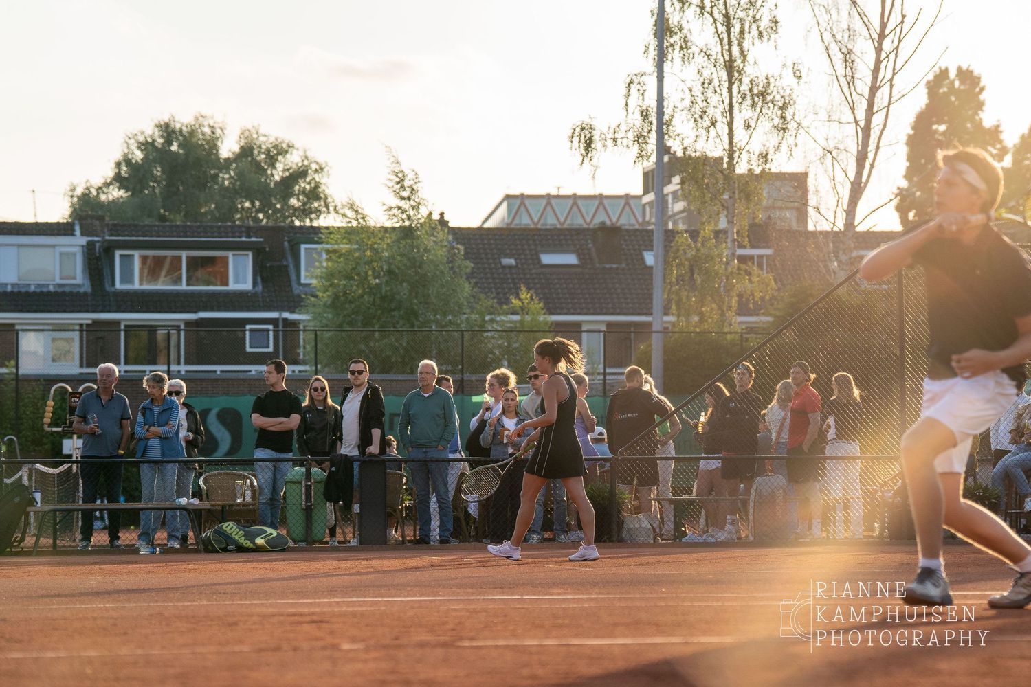Actiefoto's van de woensdagavond van eengravel tennistoernooi met spelers in actie, dubbelspel, toeschouwers en zomerse sfeer rond de baan.