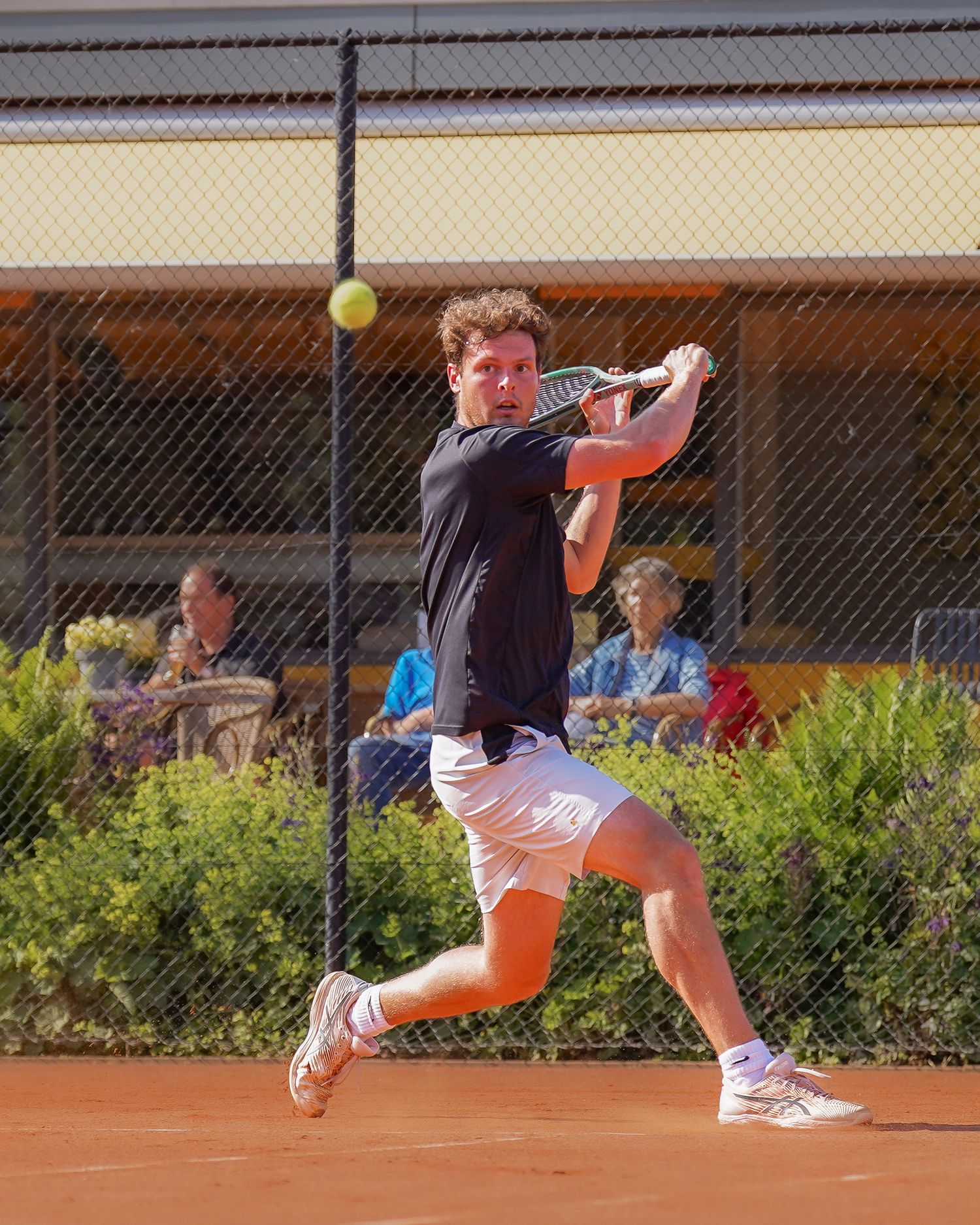 Speler in zwart shirt en witte shorts slaat een backhand terwijl hij zijn lichaam volledig meedraait.