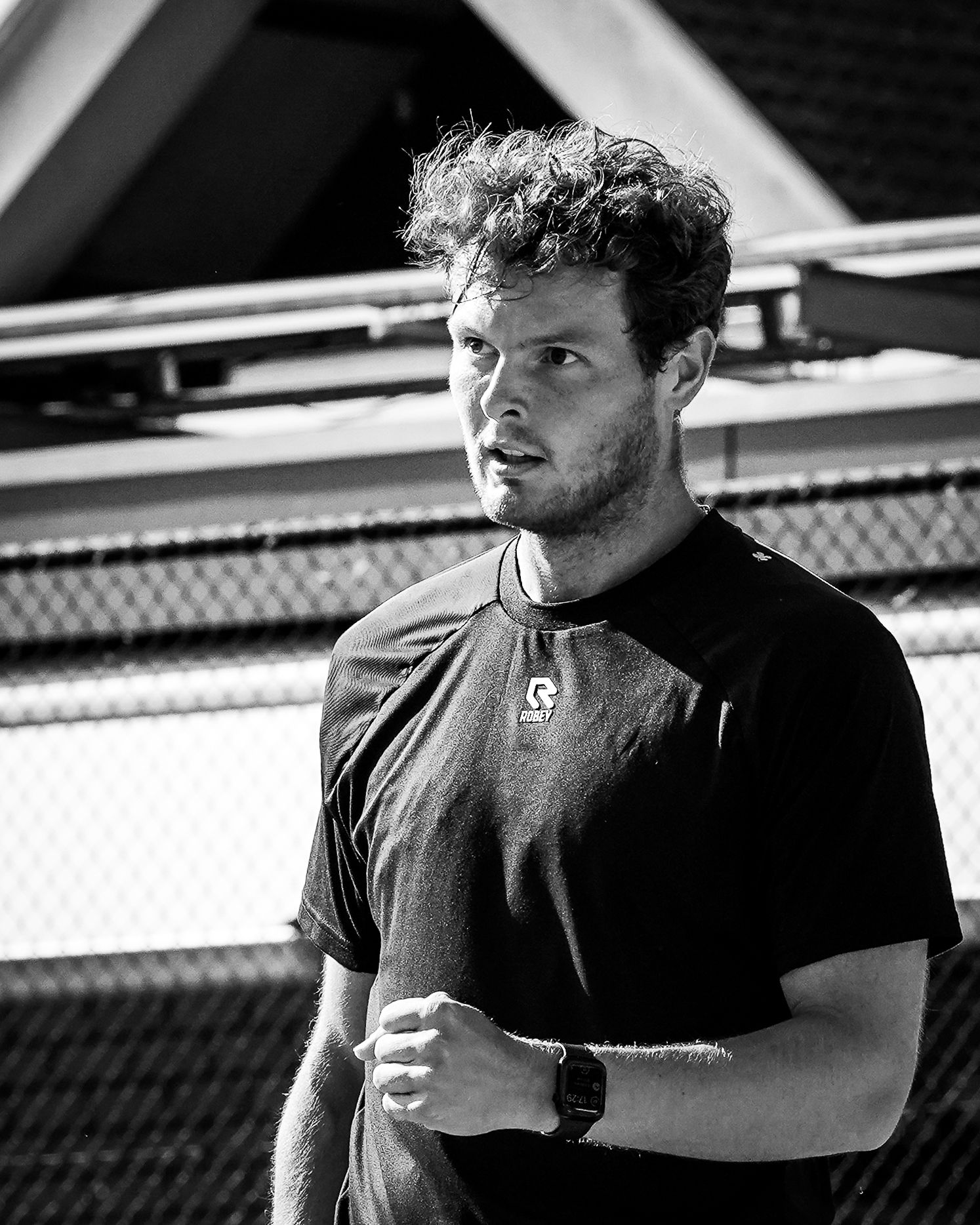 Close-up van een tennisser in zwart shirt met intense blik, vuist gebald in een moment van concentratie.