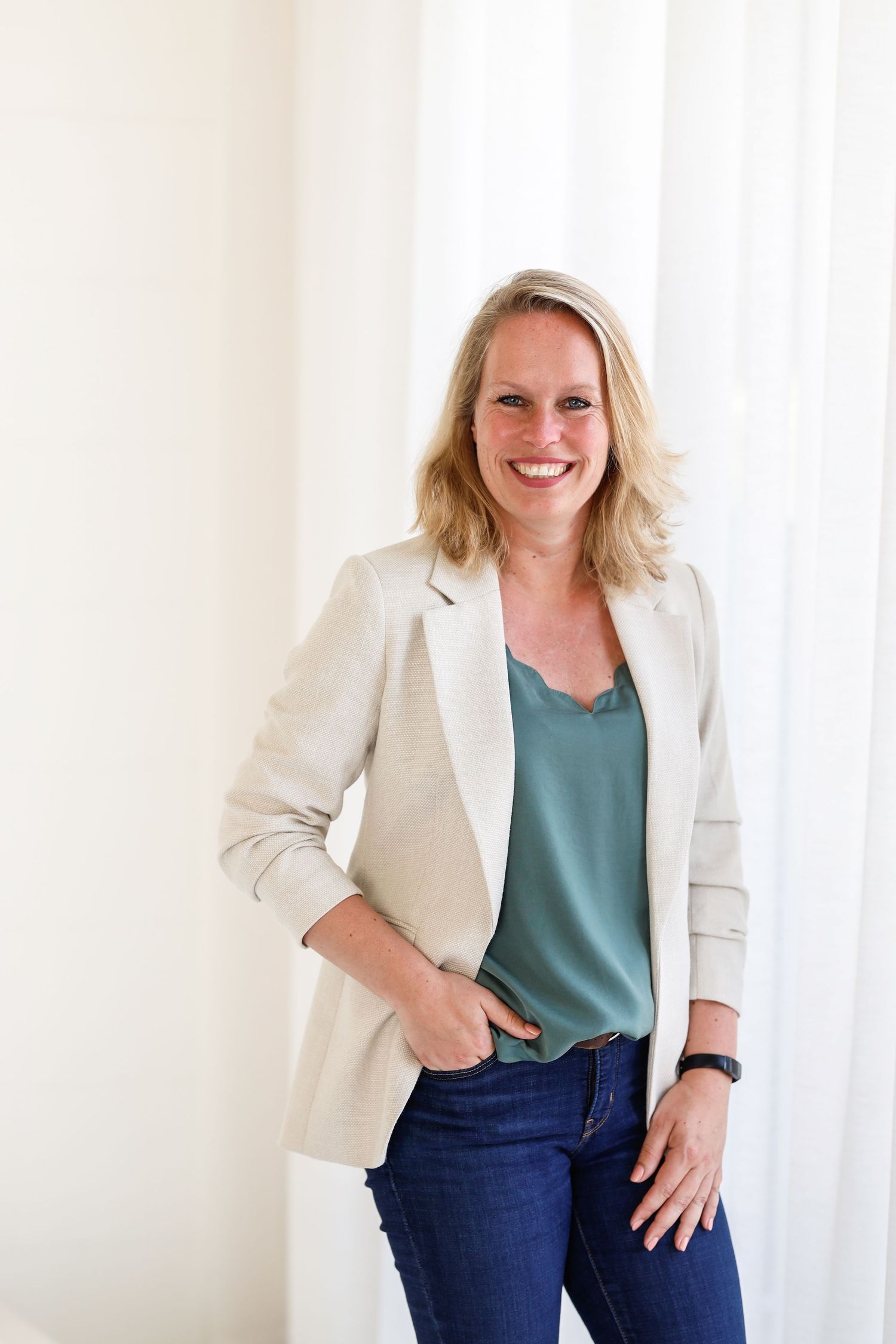 Vrouw poseert ontspannen voor lichte achtergrond in casual zakelijke kleding