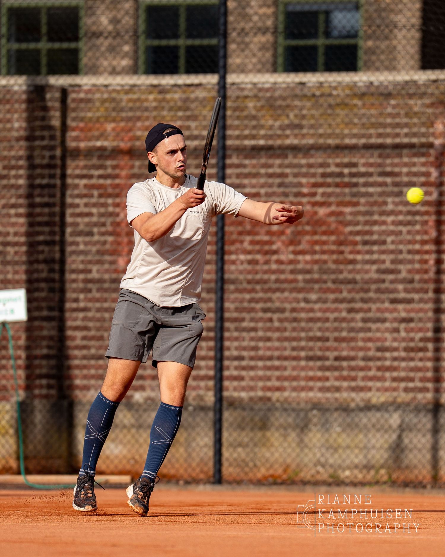 Actiefoto's van de vrijdagavond van een gravel tennistoernooi met spelers in actie, dubbelspel, toeschouwers en zomerse sfeer rond de baan.