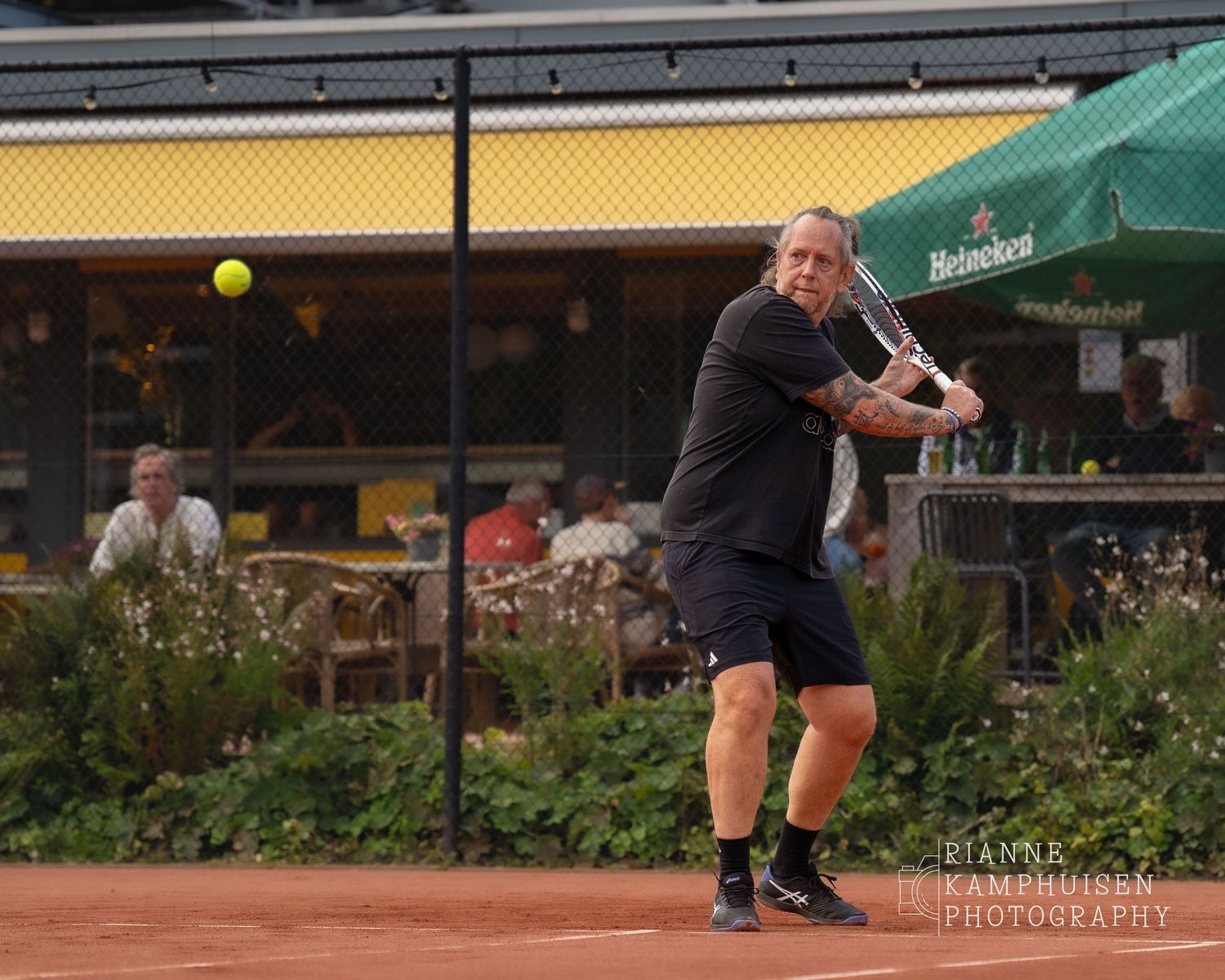 Actiefoto's van de vrijdagavond van een gravel tennistoernooi met spelers in actie, dubbelspel, toeschouwers en zomerse sfeer rond de baan.
