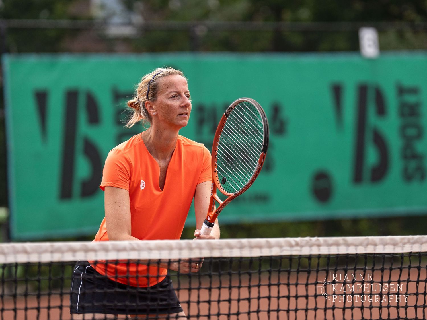 Actiefoto's van de vrijdagavond van een gravel tennistoernooi met spelers in actie, dubbelspel, toeschouwers en zomerse sfeer rond de baan.