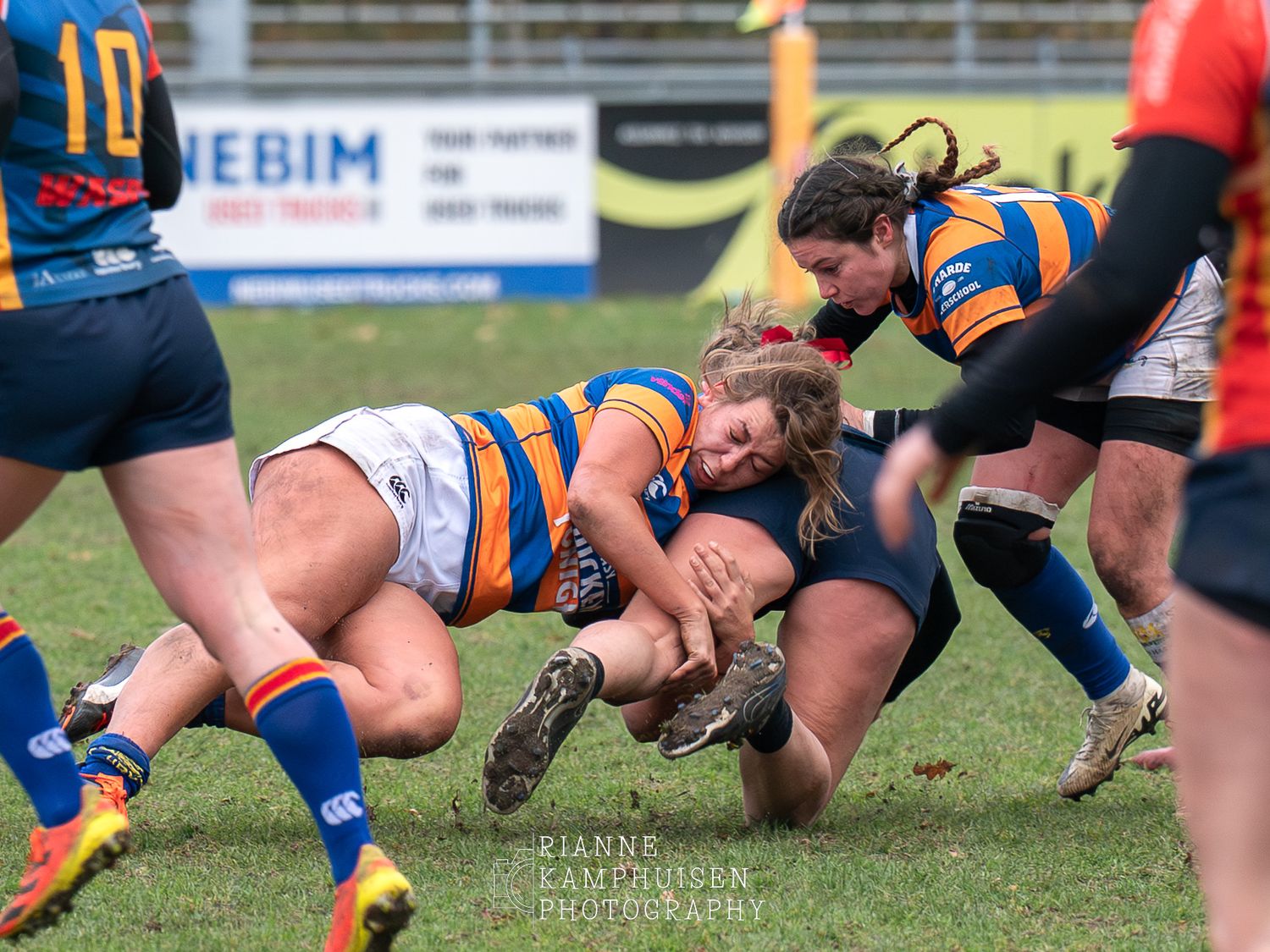 Rugby speler wordt vol getackeld door tegenstander, ze gaan beiden languit op het veld.