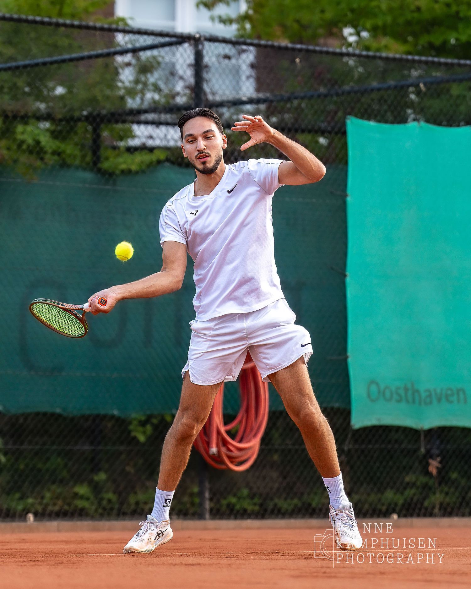 Actiefoto's van de vrijdagavond van een gravel tennistoernooi met spelers in actie, dubbelspel, toeschouwers en zomerse sfeer rond de baan.