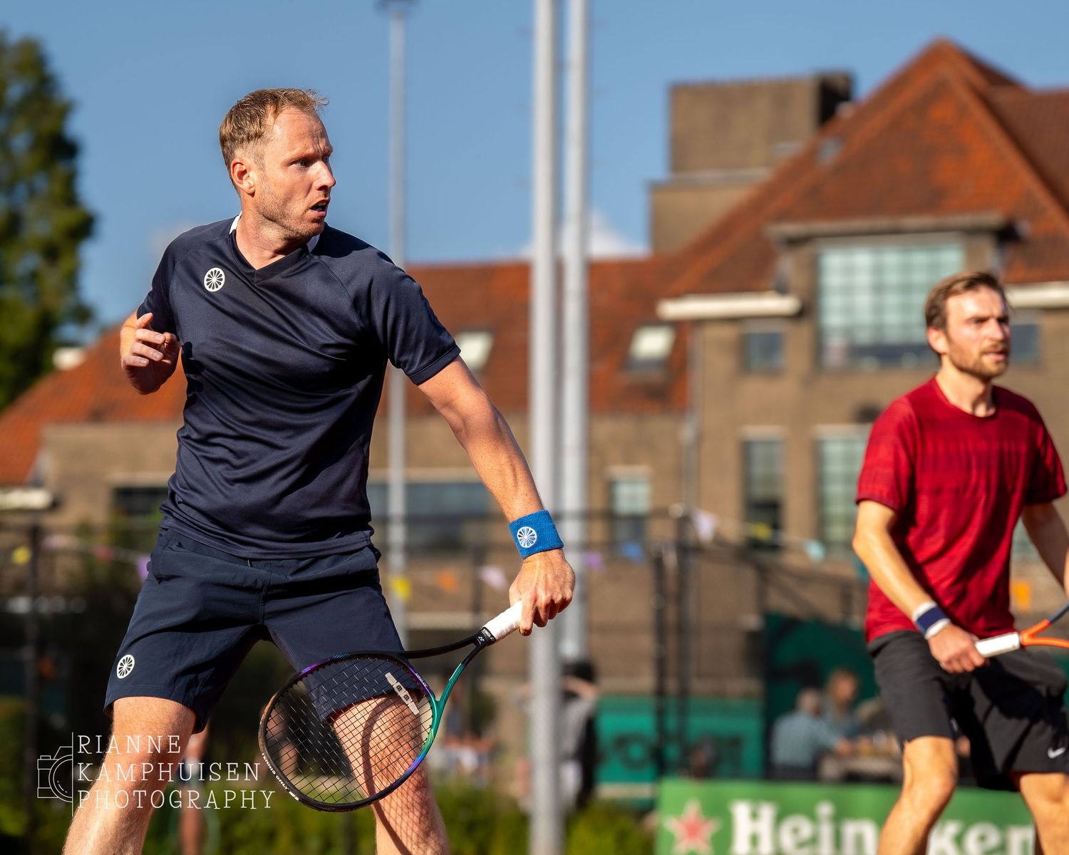 Actiefoto's van gravel tennistoernooi met spelers in actie, dubbelspel, toeschouwers en zomerse sfeer rond de baan.