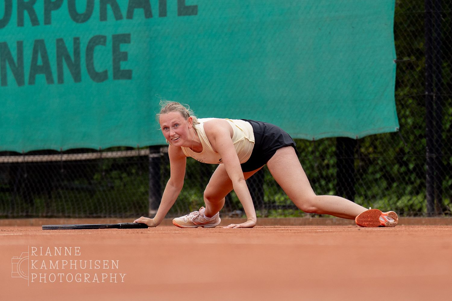 Tennisster is gevallen tijdens een punt maar lacht terwijl ze zichzelf met haar handen omhoog duwt.