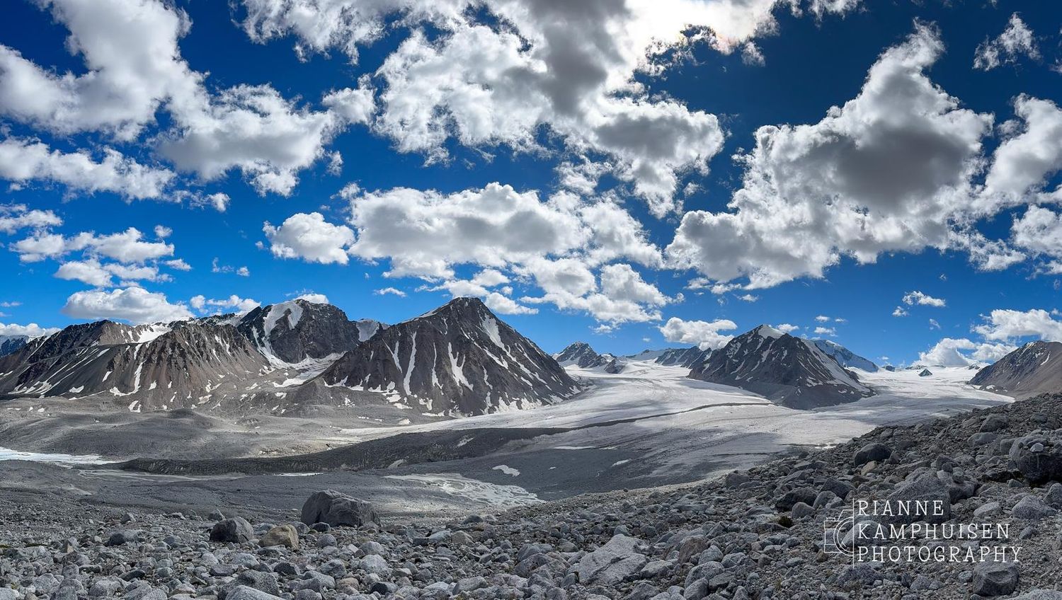 Uitzicht op een uitgestrekt berglandschap met besneeuwde toppen en gletsjers onder een heldere blauwe lucht met wolken. Altai, Mongolie