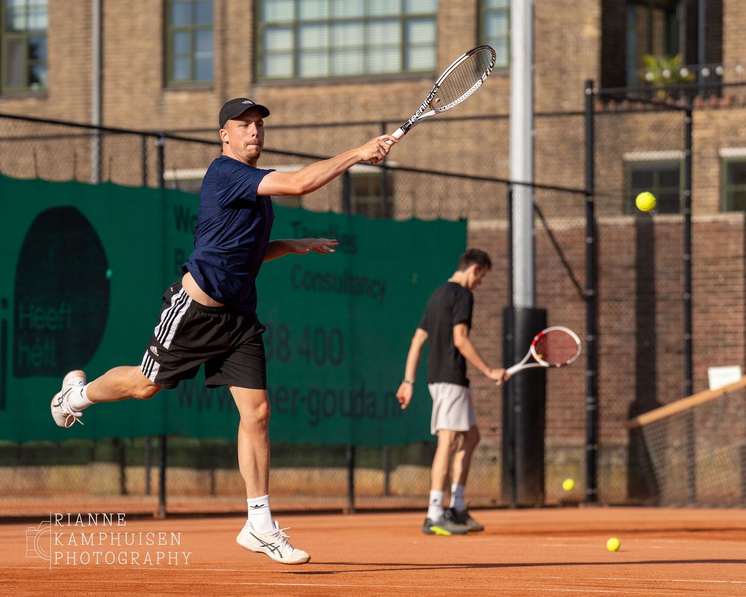 Actiefoto's van gravel tennistoernooi met spelers in actie, dubbelspel, toeschouwers en zomerse sfeer rond de baan.