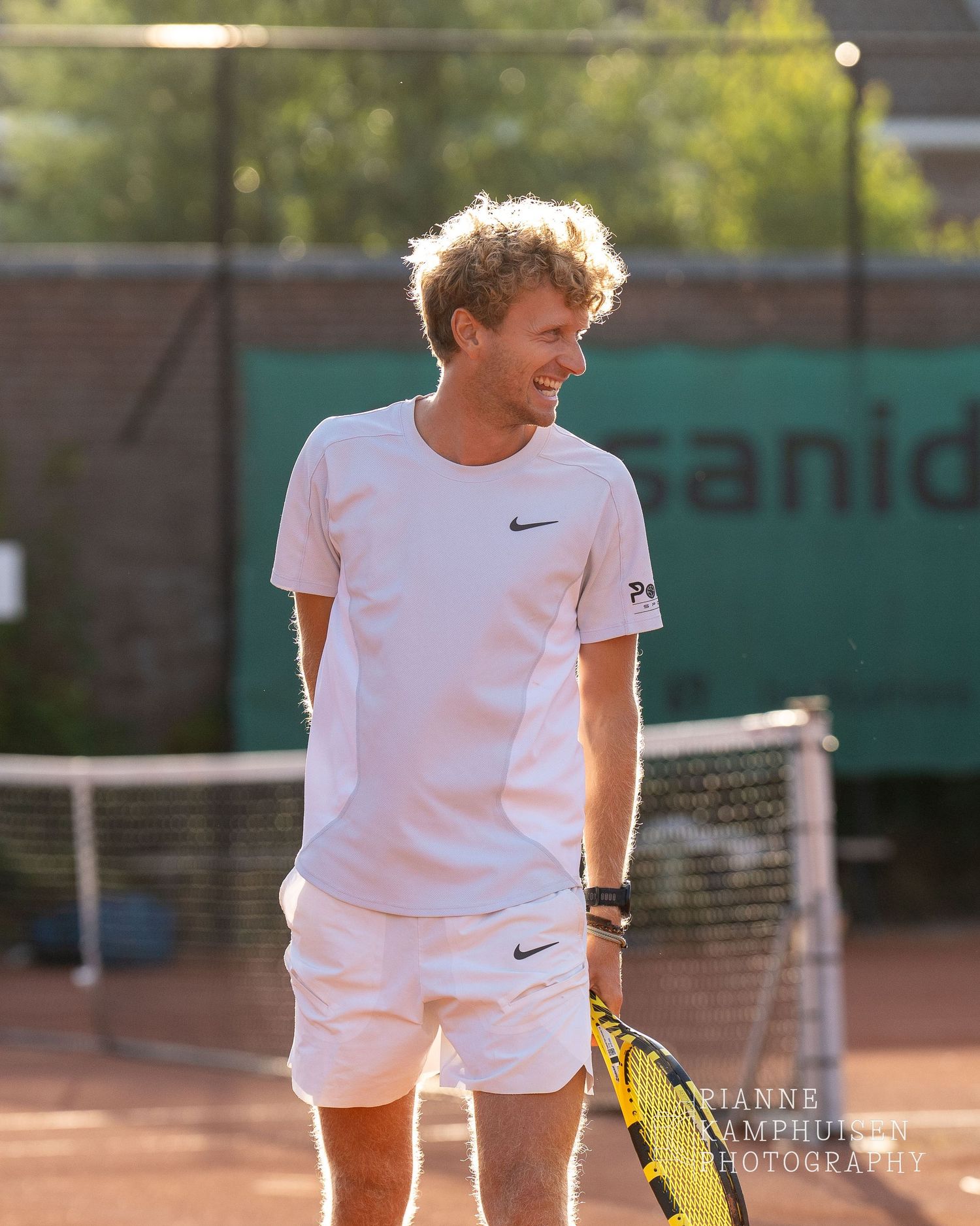 Actiefoto's van de vrijdagavond van een gravel tennistoernooi met spelers in actie, dubbelspel, toeschouwers en zomerse sfeer rond de baan.