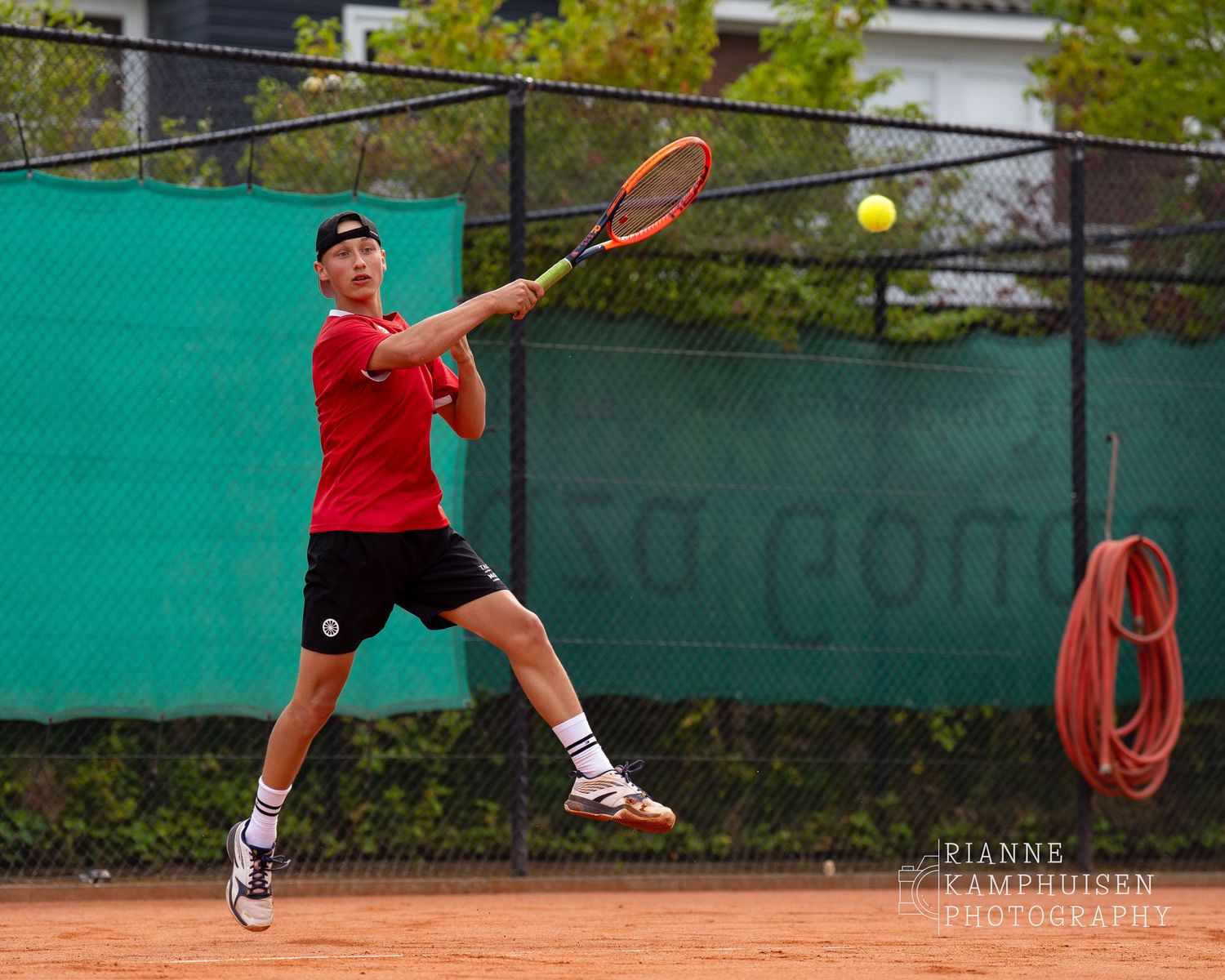 Actiefoto's van de vrijdagavond van een gravel tennistoernooi met spelers in actie, dubbelspel, toeschouwers en zomerse sfeer rond de baan.