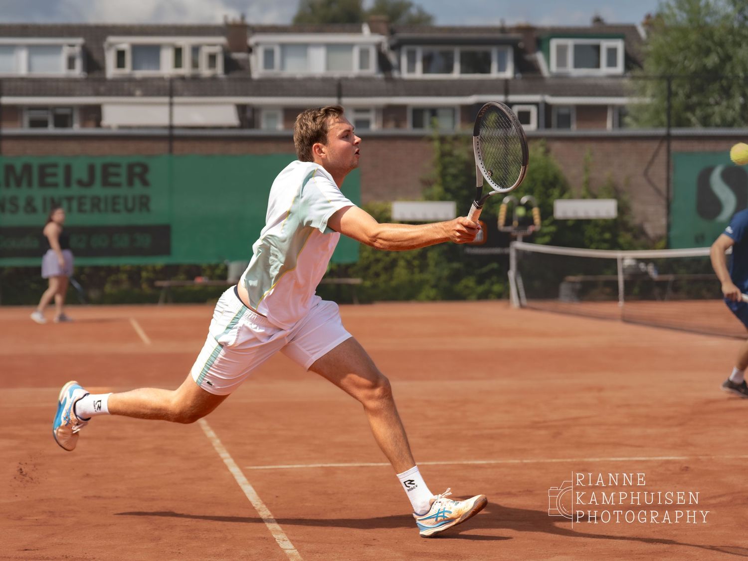 Speler rent op een gravel tennisbaan naar voren om een bal te slaan