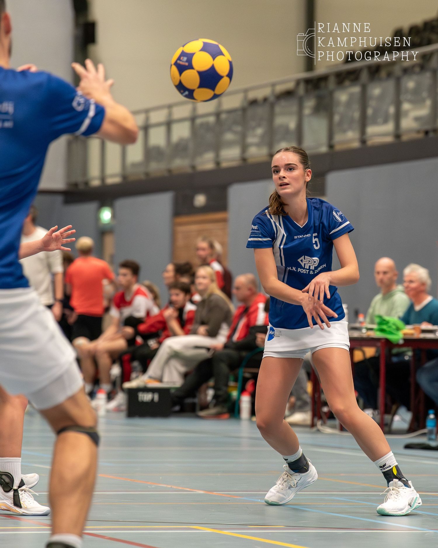 Vrouwelijke korfbalspeler passt een bal naar een andere speler in een grote sporthal