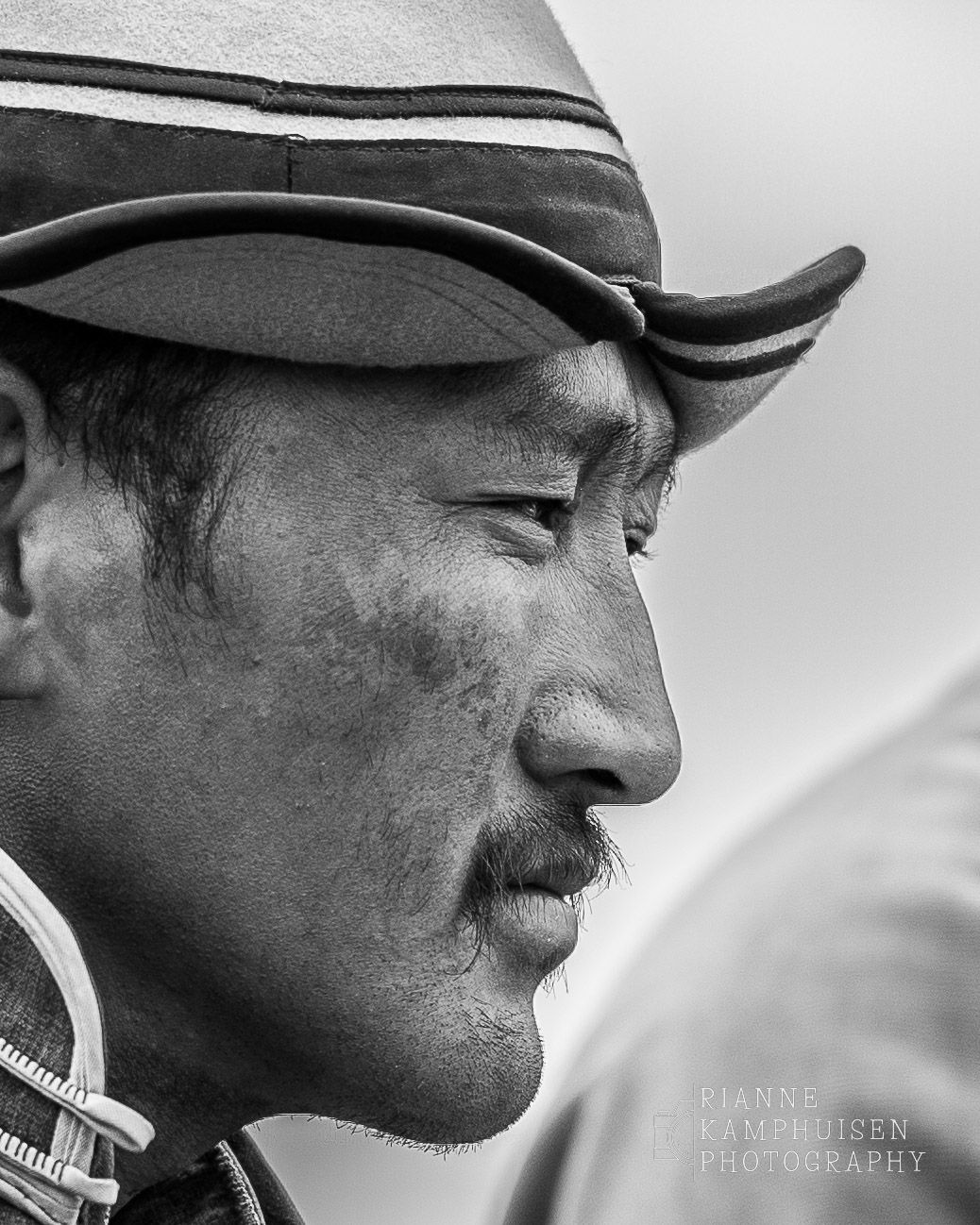 Zwart-wit portret van een Mongoolse man in profiel, gekleed in traditionele kleding en hoofddeksel.