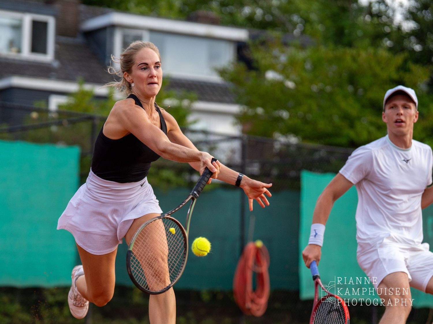 Actiefoto's van gravel tennistoernooi met spelers in actie, dubbelspel, toeschouwers en zomerse sfeer rond de baan.
