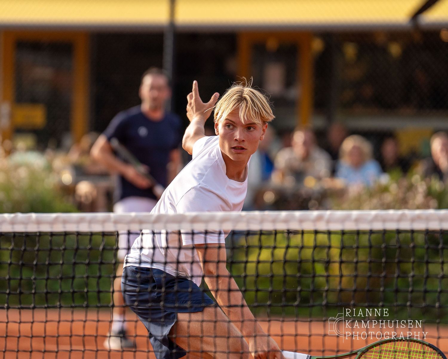 Actiefoto's van de vrijdagavond van een gravel tennistoernooi met spelers in actie, dubbelspel, toeschouwers en zomerse sfeer rond de baan.