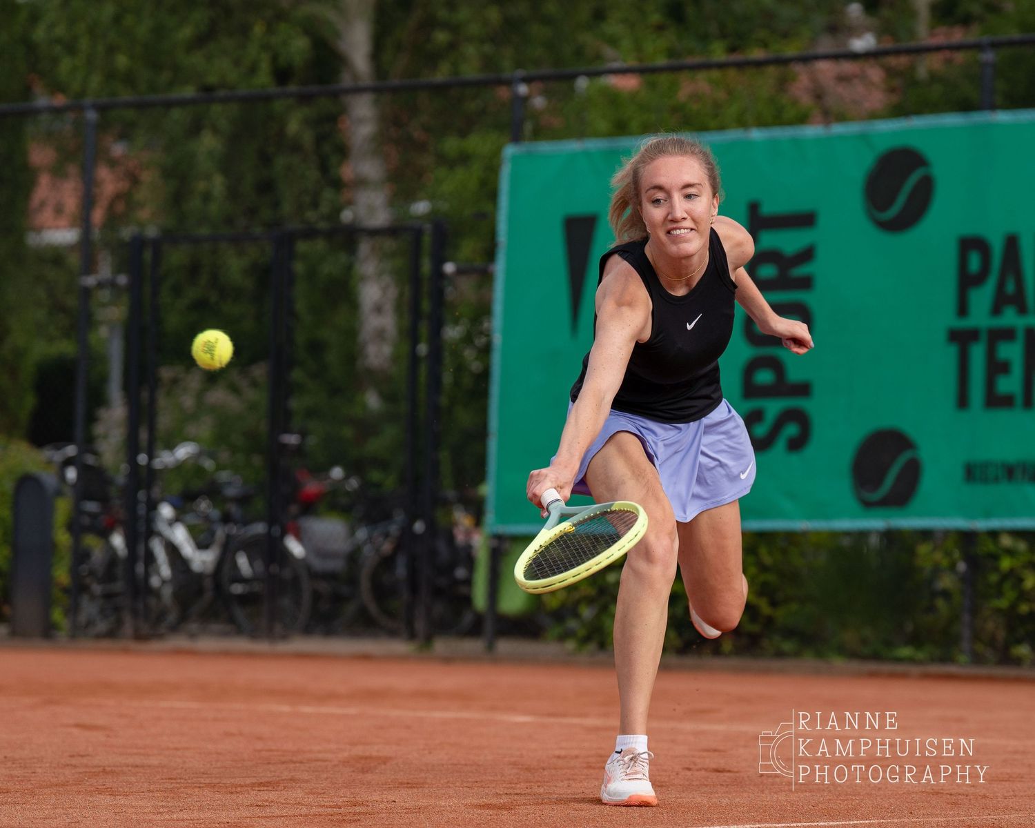 Actiefoto's van de vrijdagavond van een gravel tennistoernooi met spelers in actie, dubbelspel, toeschouwers en zomerse sfeer rond de baan.
