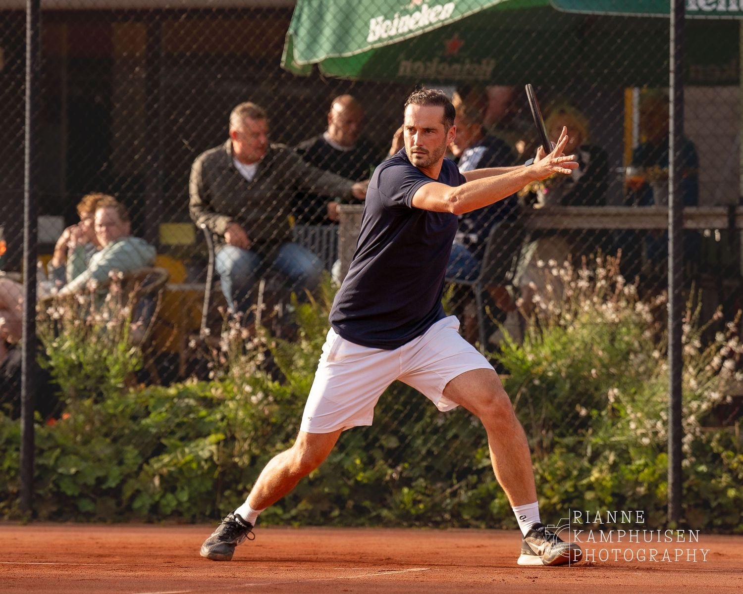 Actiefoto's van de vrijdagavond van een gravel tennistoernooi met spelers in actie, dubbelspel, toeschouwers en zomerse sfeer rond de baan.
