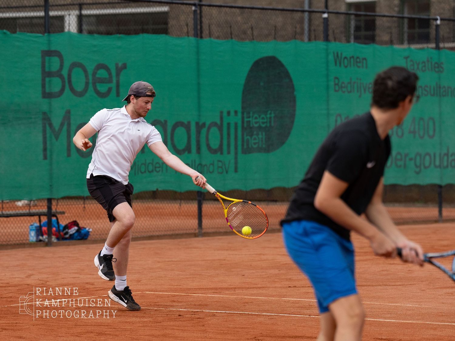 Actiefoto's en finalisten van een gravel tennistoernooi met spelers in actie, dubbelspel, toeschouwers en zomerse sfeer rond de baan.