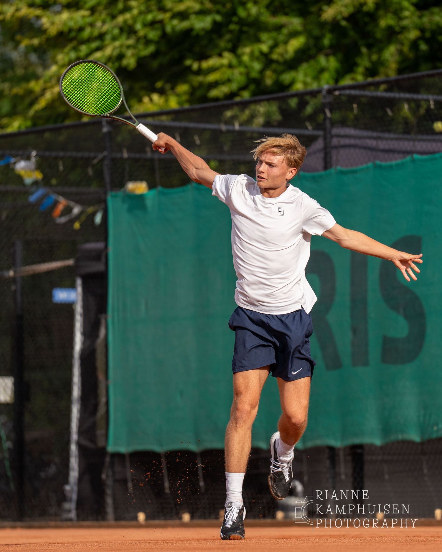 Actiefoto's van de vrijdagavond van een gravel tennistoernooi met spelers in actie, dubbelspel, toeschouwers en zomerse sfeer rond de baan.