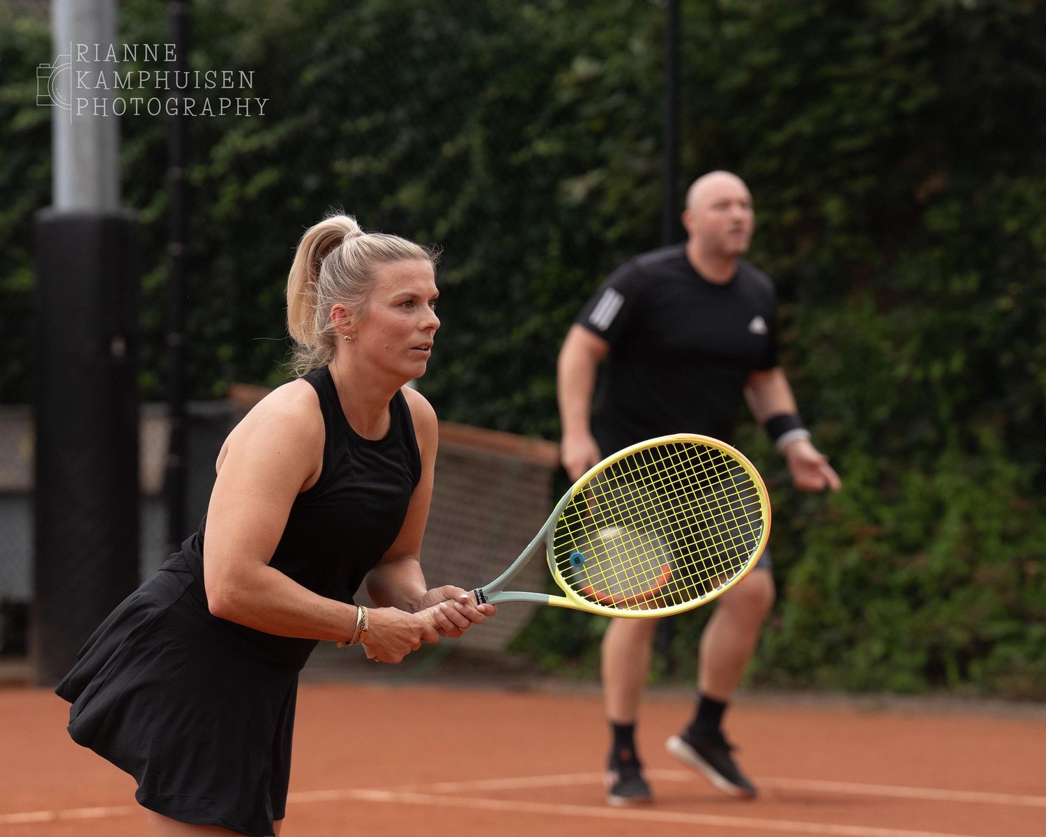 Actiefoto's van gravel tennistoernooi met spelers in actie, dubbelspel, toeschouwers en zomerse sfeer rond de baan.