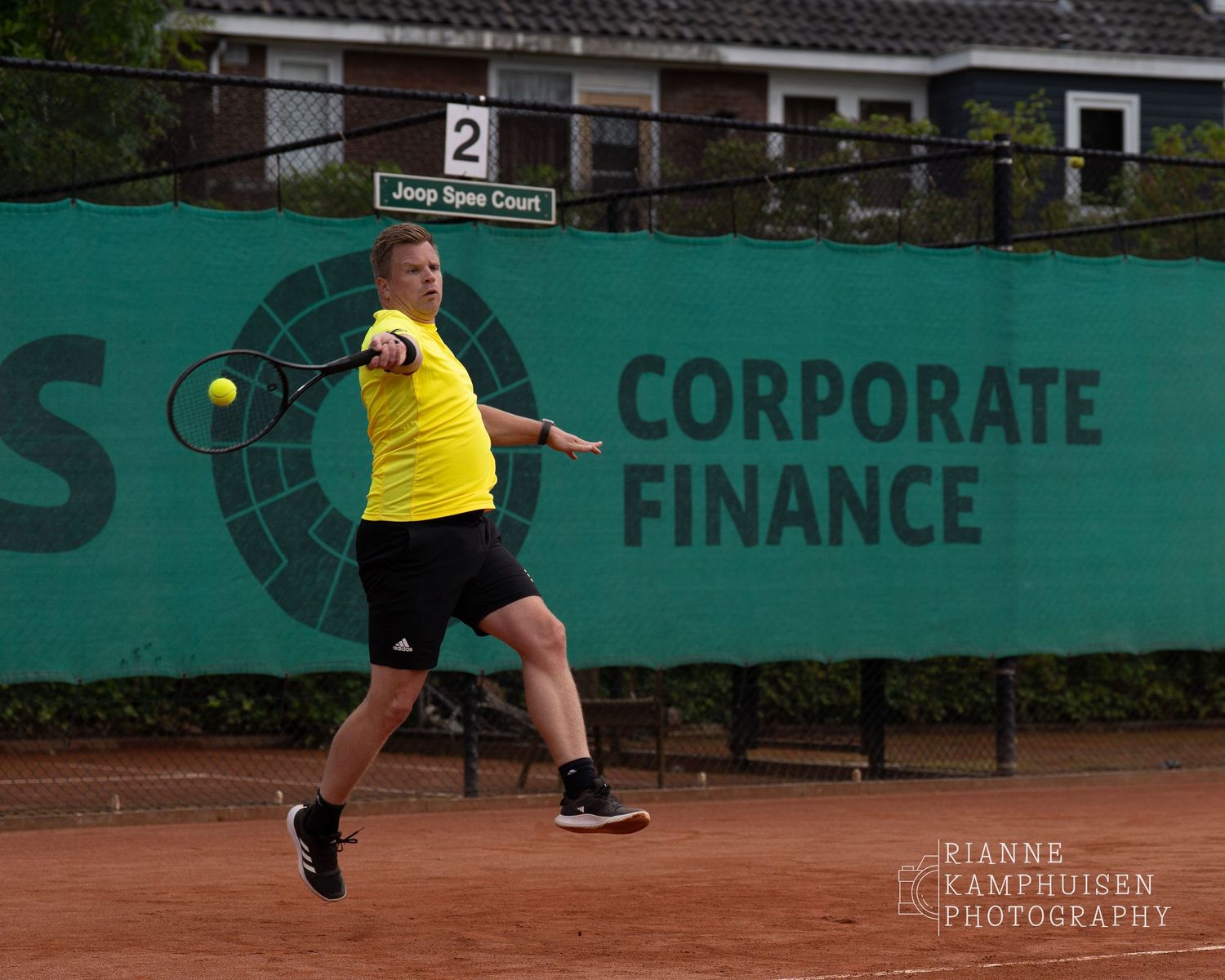 Actiefoto's van de vrijdagavond van een gravel tennistoernooi met spelers in actie, dubbelspel, toeschouwers en zomerse sfeer rond de baan.