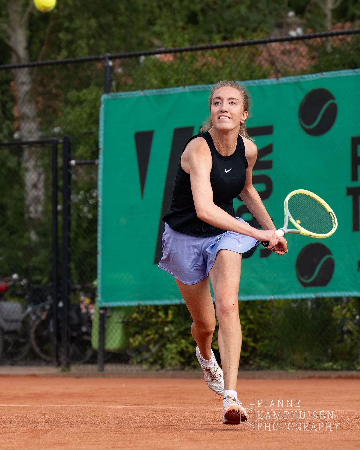 Actiefoto's van de vrijdagavond van een gravel tennistoernooi met spelers in actie, dubbelspel, toeschouwers en zomerse sfeer rond de baan.