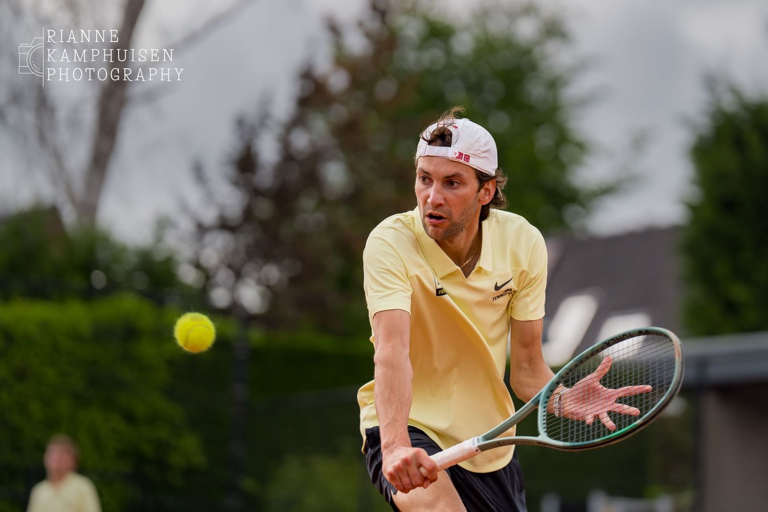 Speler in lichtgeel shirt kijkt scherp naar de bal tijdens een lage volley, met het racket klaar voor contact.