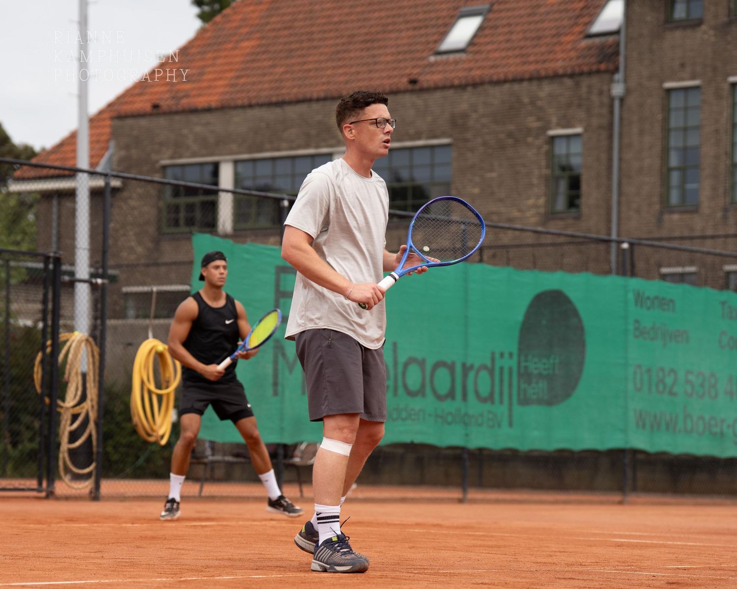 Actiefoto's van gravel tennistoernooi met spelers in actie, dubbelspel, toeschouwers en zomerse sfeer rond de baan.
