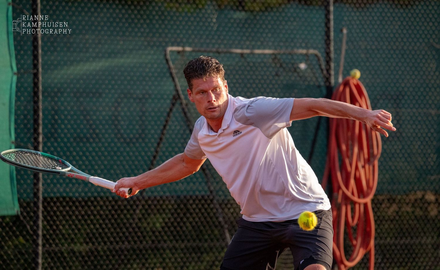 Tennisser geconcentreerd in afslagpositie, klaar om een bal met zijn forehand te raken op een zonnige baan.