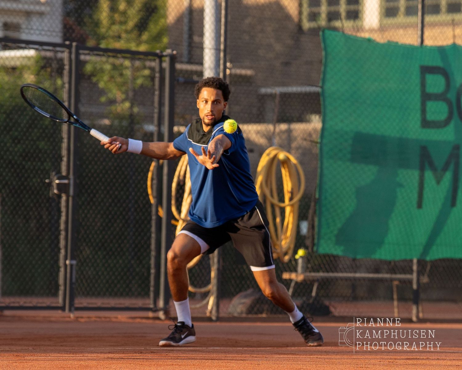 Actiefoto's van de vrijdagavond van een gravel tennistoernooi met spelers in actie, dubbelspel, toeschouwers en zomerse sfeer rond de baan.
