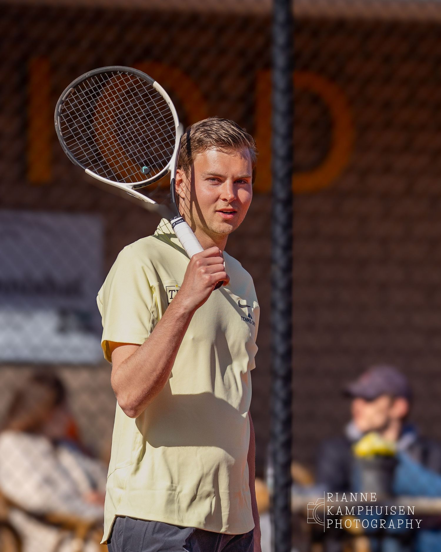 Tennisser kijkt richting de camera met een ontspannen blik, racket rustend op zijn schouder.