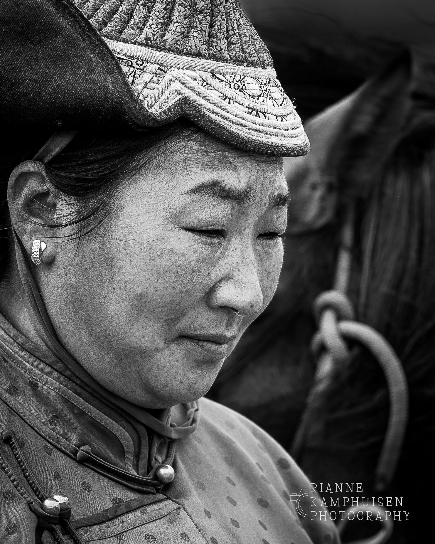 Portret van een vrouw in traditionele Mongoolse kleding en hoofddeksel, met een ingetogen uitdrukking, in zwart-wit.