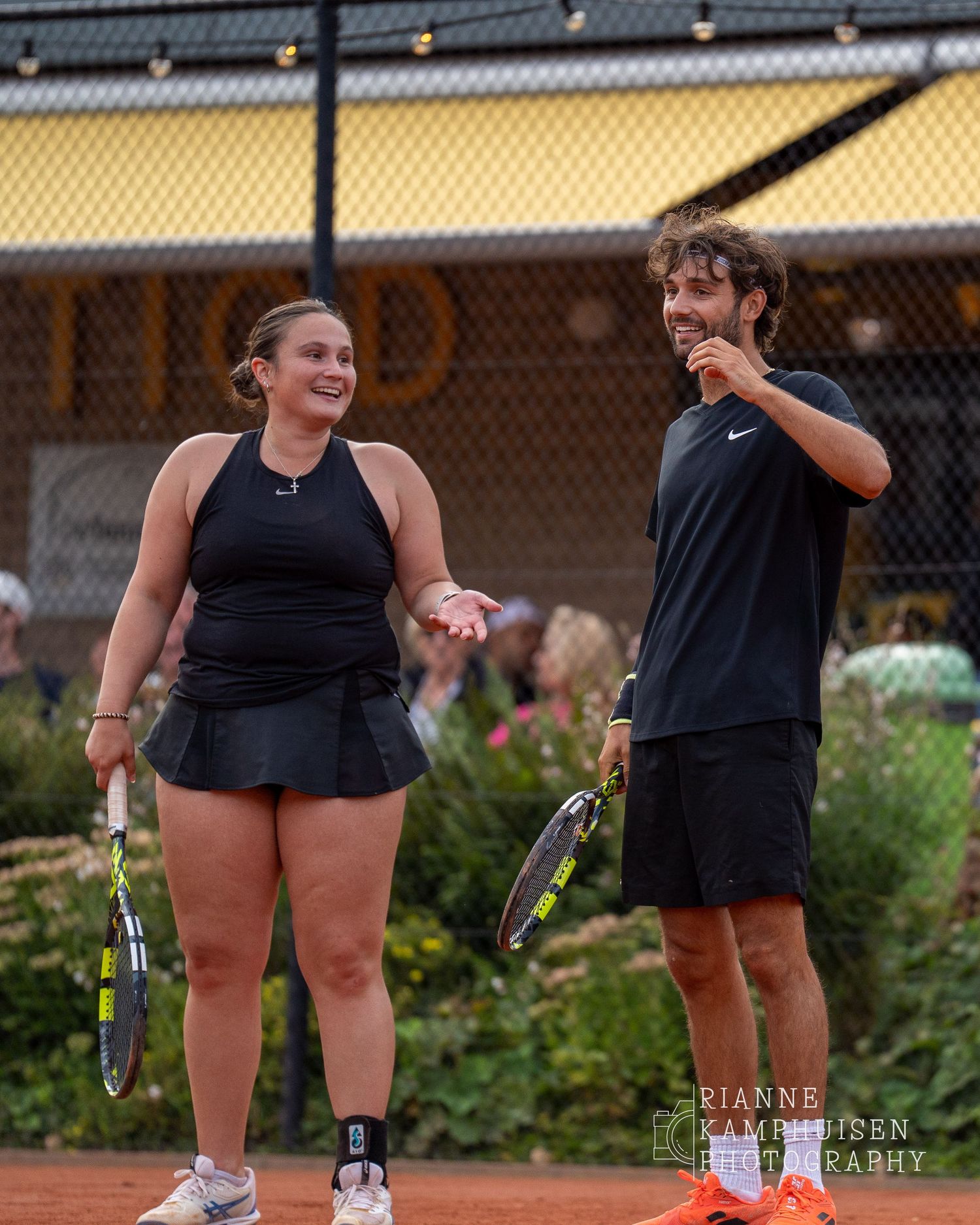 Actiefoto's van gravel tennistoernooi met spelers in actie, dubbelspel, toeschouwers en zomerse sfeer rond de baan.