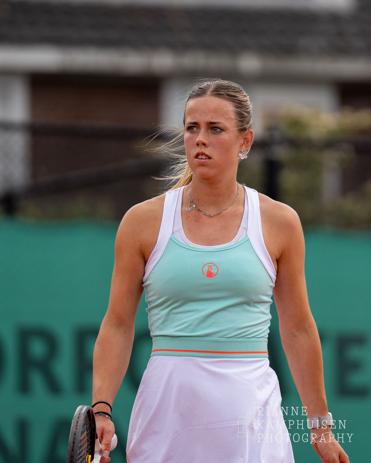 Tennisster in mintgroen sporttopje kijkt gefocust vooruit tijdens een wedstrijd op een gravelbaan.