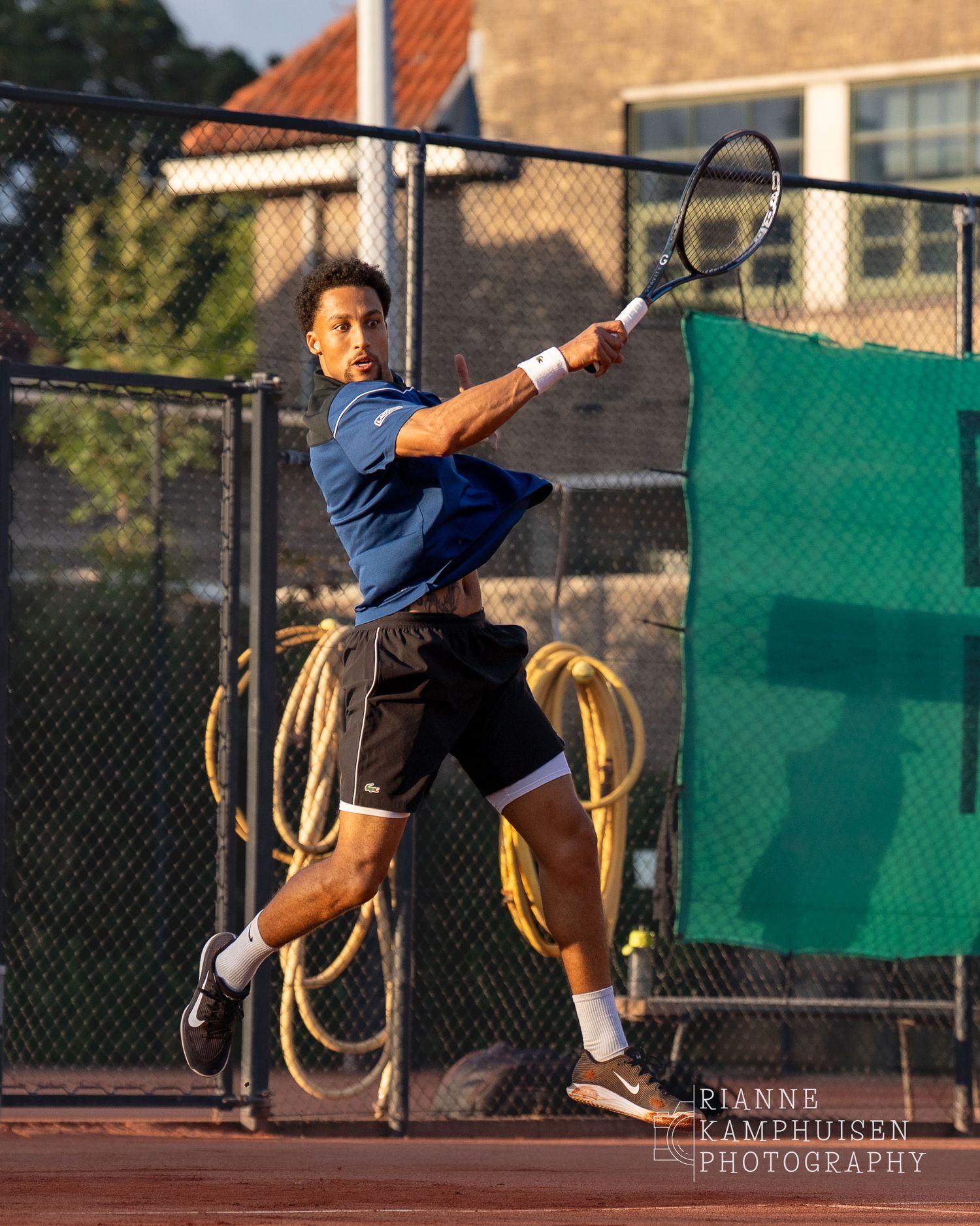 Actiefoto's van de vrijdagavond van een gravel tennistoernooi met spelers in actie, dubbelspel, toeschouwers en zomerse sfeer rond de baan.